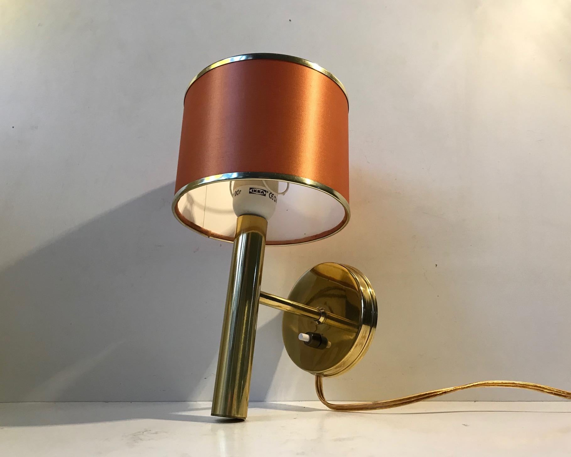 Fixed wall light designed and manufactured by Svend Mejlstrøm in Denmark during the 1960s. It’s made from polished brass and retains its peach colored textile shade that came with it originally.