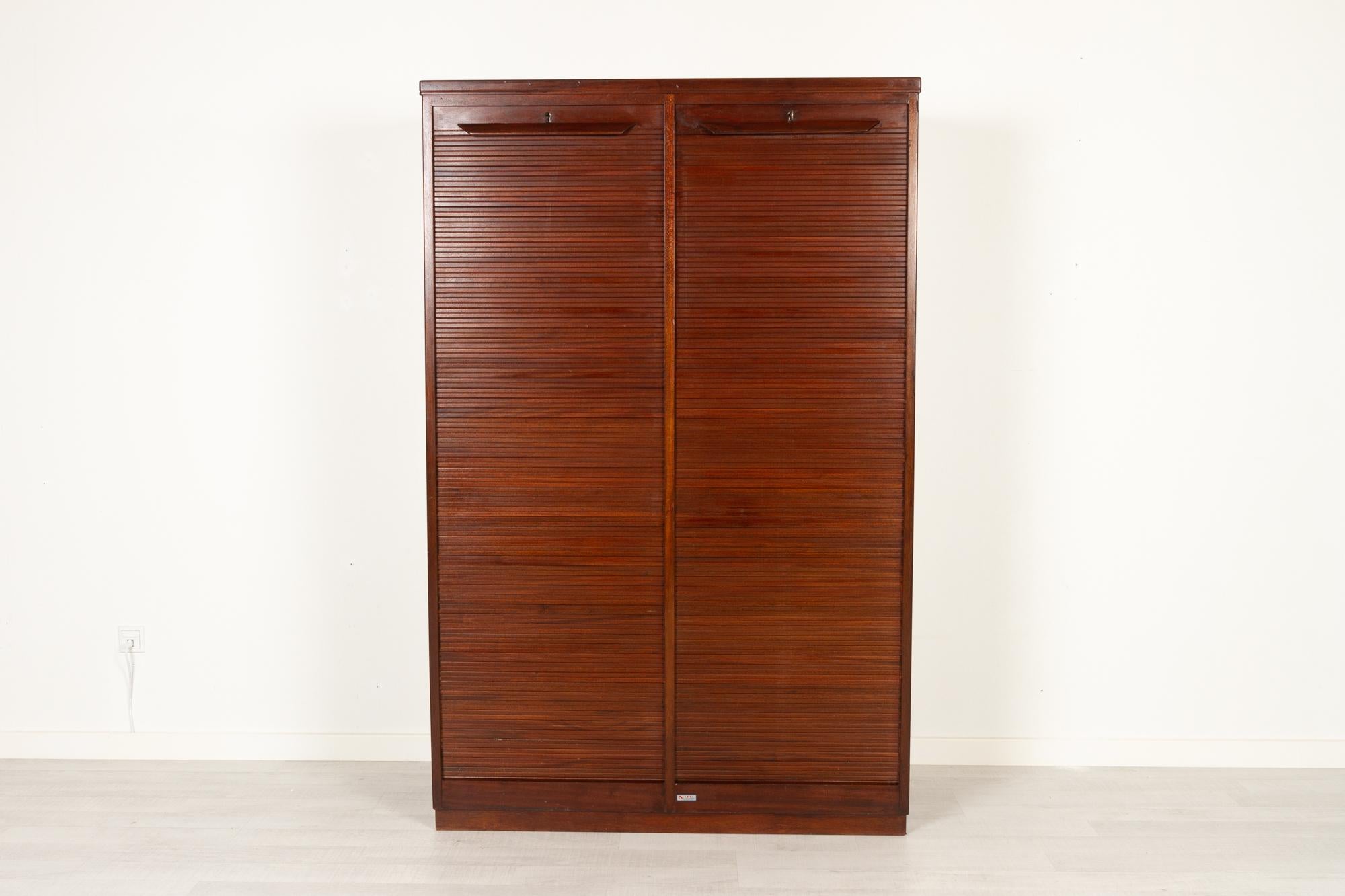 Vintage Danish cabinet with tambour doors by Nipu, Denmark 1950s
Large double filing cabinet with vertical tambour doors in stained hardwood. Two compartments with a total of twelve shelves of which ten are adjustable/removable. One key is