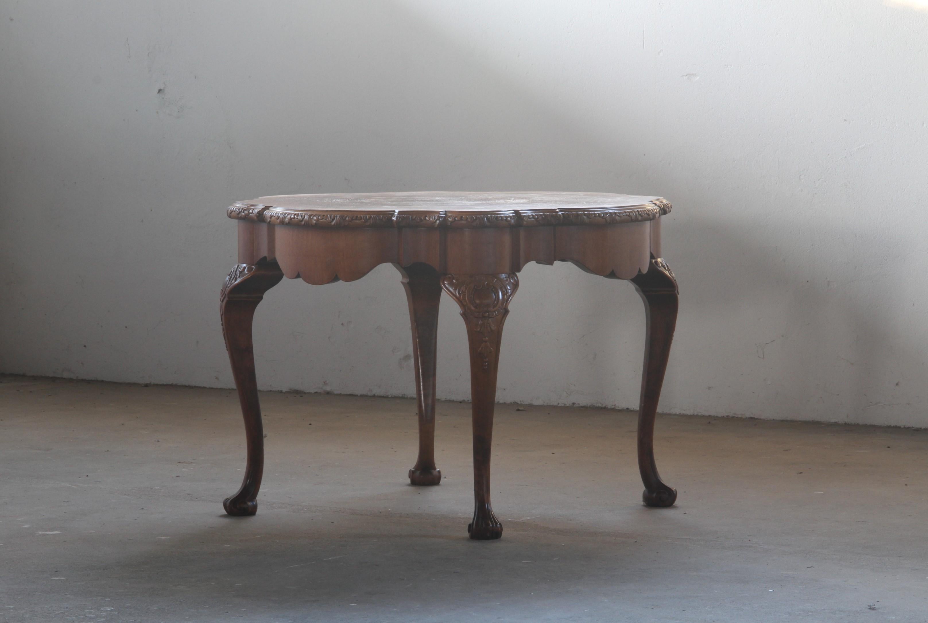Cette table basse vintage est une pièce unique, mêlant l'artisanat danois à l'influence élégante du style Louis XV antique français. Son design distinctif se caractérise par des pieds en forme de griffes et des motifs sculptés de manière complexe