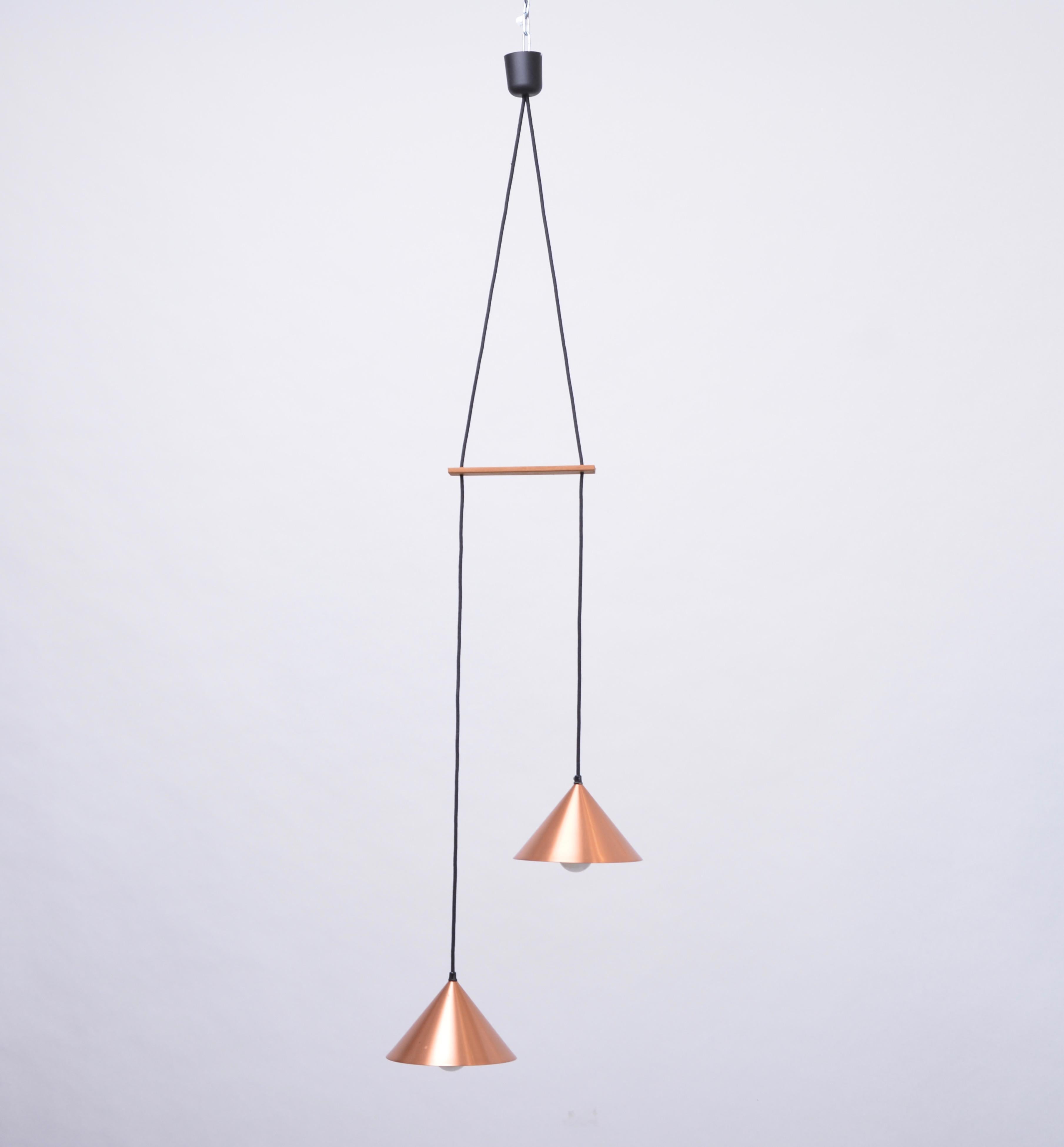 Danish Mid-Century Modern Copper colored Pendant light

This pendant light consists of two-cone shaped lamp shades made from copper plated aluminium. A piece of wood keeps the two lamps separated. The cable is black textile cable. The lamp was made