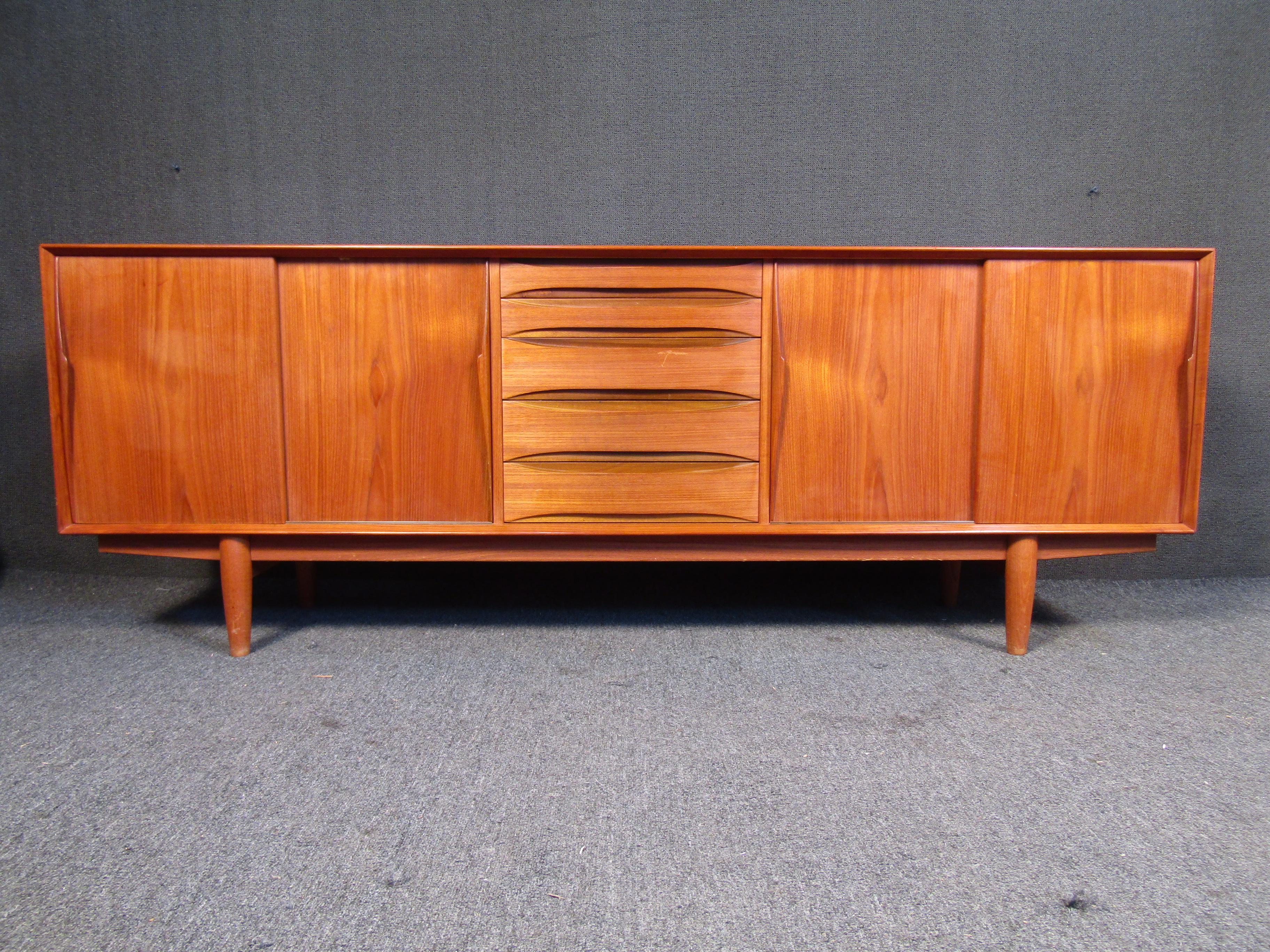 This large Mid-Century Modern credenza by Dyrlund combines quality materials like rich teak wood with a stylish vintage design and Danish craftsmanship. This unusually wide piece offers extra storage for any room or office in a timeless Mid-Century