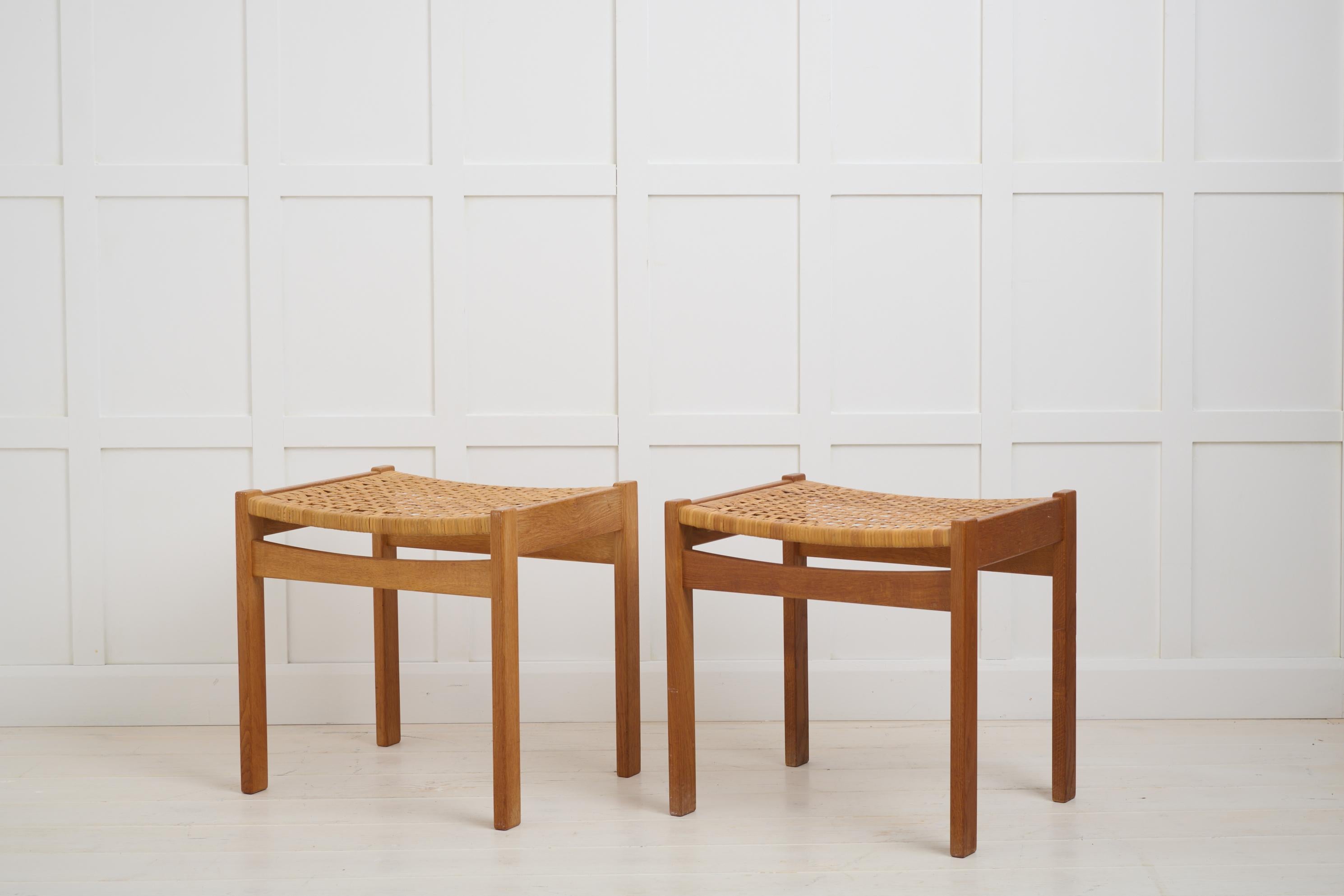 Un par de reposapiés de diseño danés, con estructura de roble macizo y asiento de ratán. Un taburete tiene una pegatina de Illums Bolighus, Copenhague. Buen estado vintage. Los asientos de ratán están algo desgastados. 