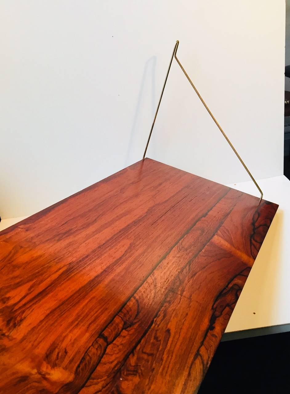 Large floating wall shelf (85x32 cm) composed of a Rio Rosewood veneered shelf suspended via brass mounts to each side. It was manufactured and designed in Denmark during the 1960s in a style reminiscent of Finn Juhl, Kai Kristiansen and Poul