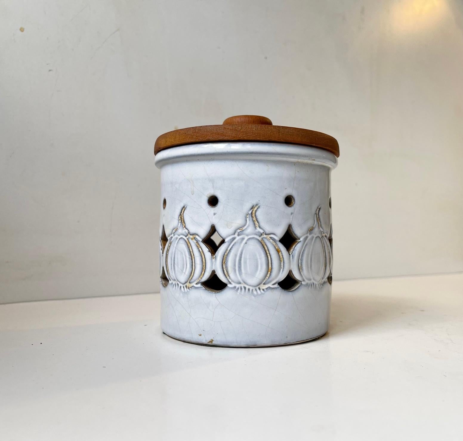 Wellmade lidded jar intended for storing garlic. Decorated in white glaze with piercings and garlics in relief. Label from Frands V. Measurements: H: 14 cm, D: 12 cm.