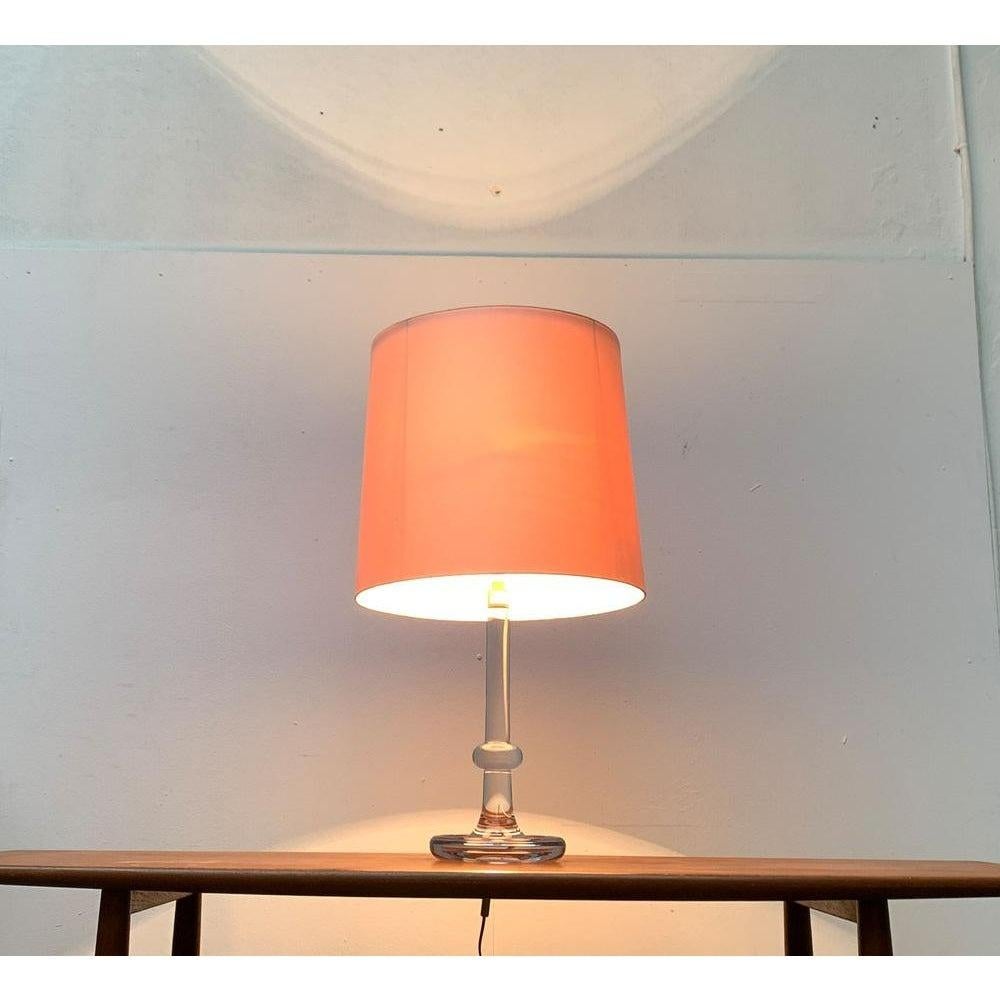 Imposante lampe de table du fabricant danois Holmegaard d'après un design de Michael Bang des années 70.

Un design avec un langage de formes traditionnel. Cette grande lampe de table convainc par son pied ornemental en verre. En revanche, une