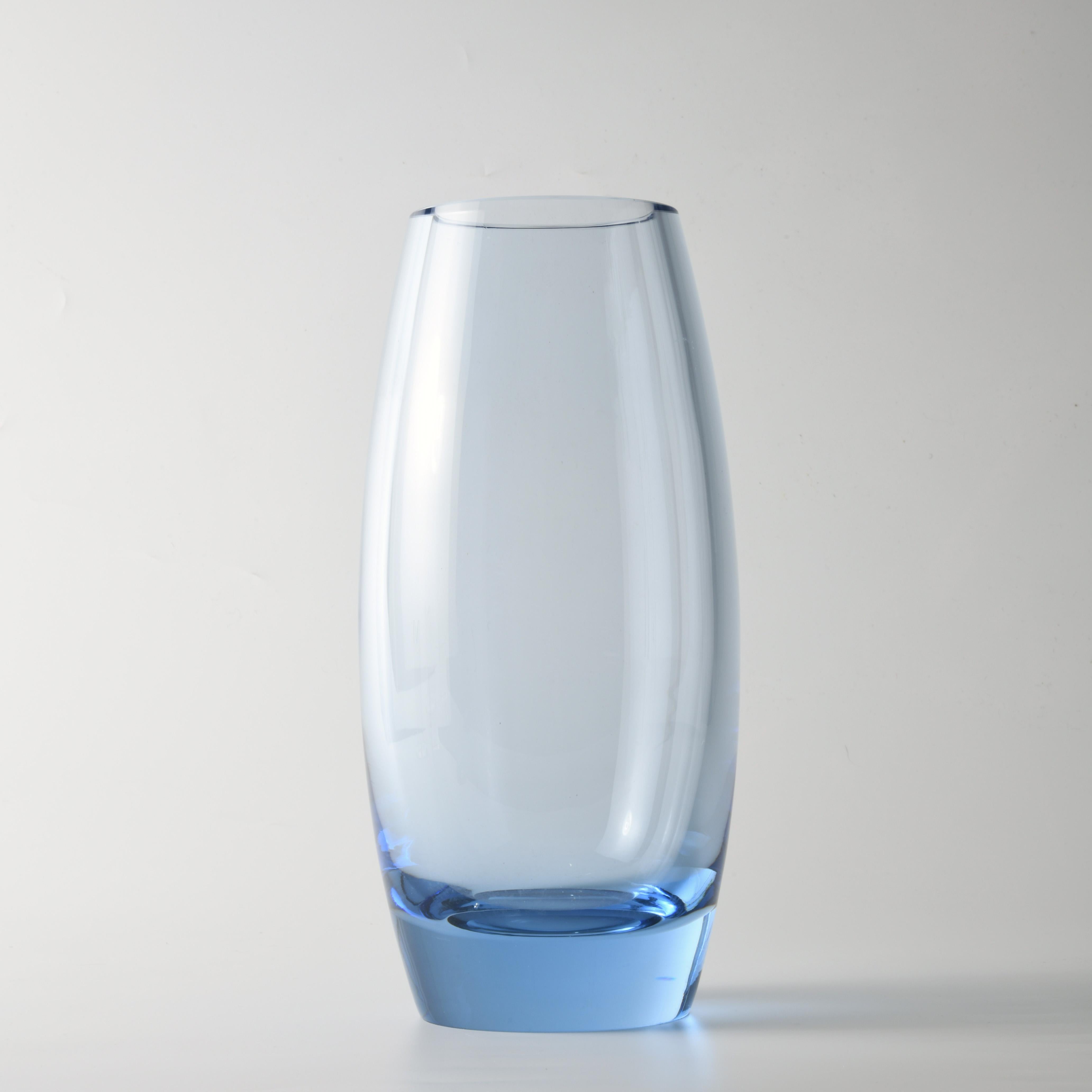 Vase en verre (H:25cm), design de Per Lutken (1916-1998), édité par la célèbre verrerie danoise Holmegaard. Le ton bleuté, l'épaisseur du verre visible au sommet font partie intégrante de la conception de ce vase, daté et signé en dessous.
Per