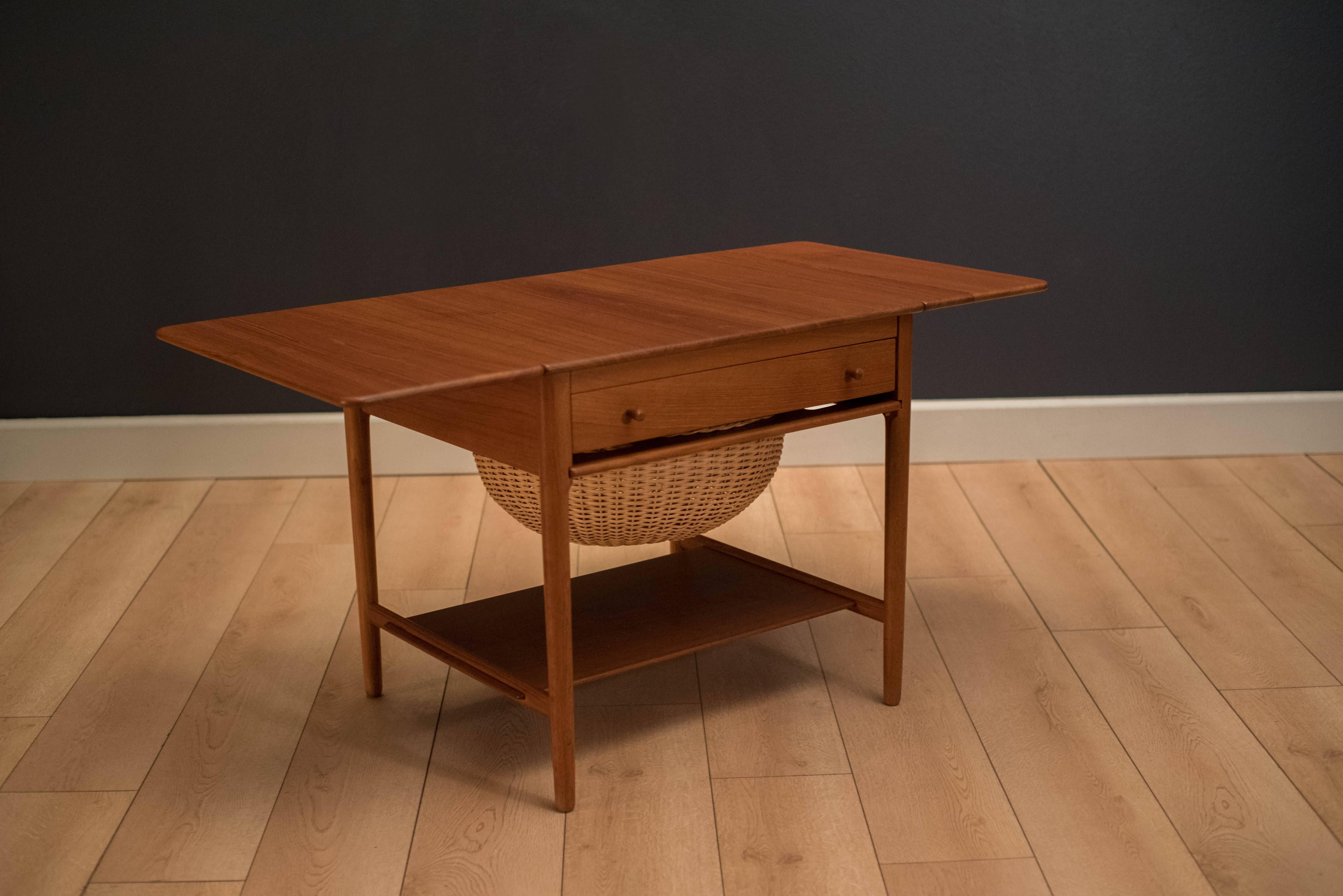 Mid century Danish sewing table designed by Hans Wegner for Andreas Tuck. This piece is constructed of solid teak and oak and features an extendable drop leaf tabletop. Includes one drawer and pull-out wicker basket tray. Tabletop extends out to