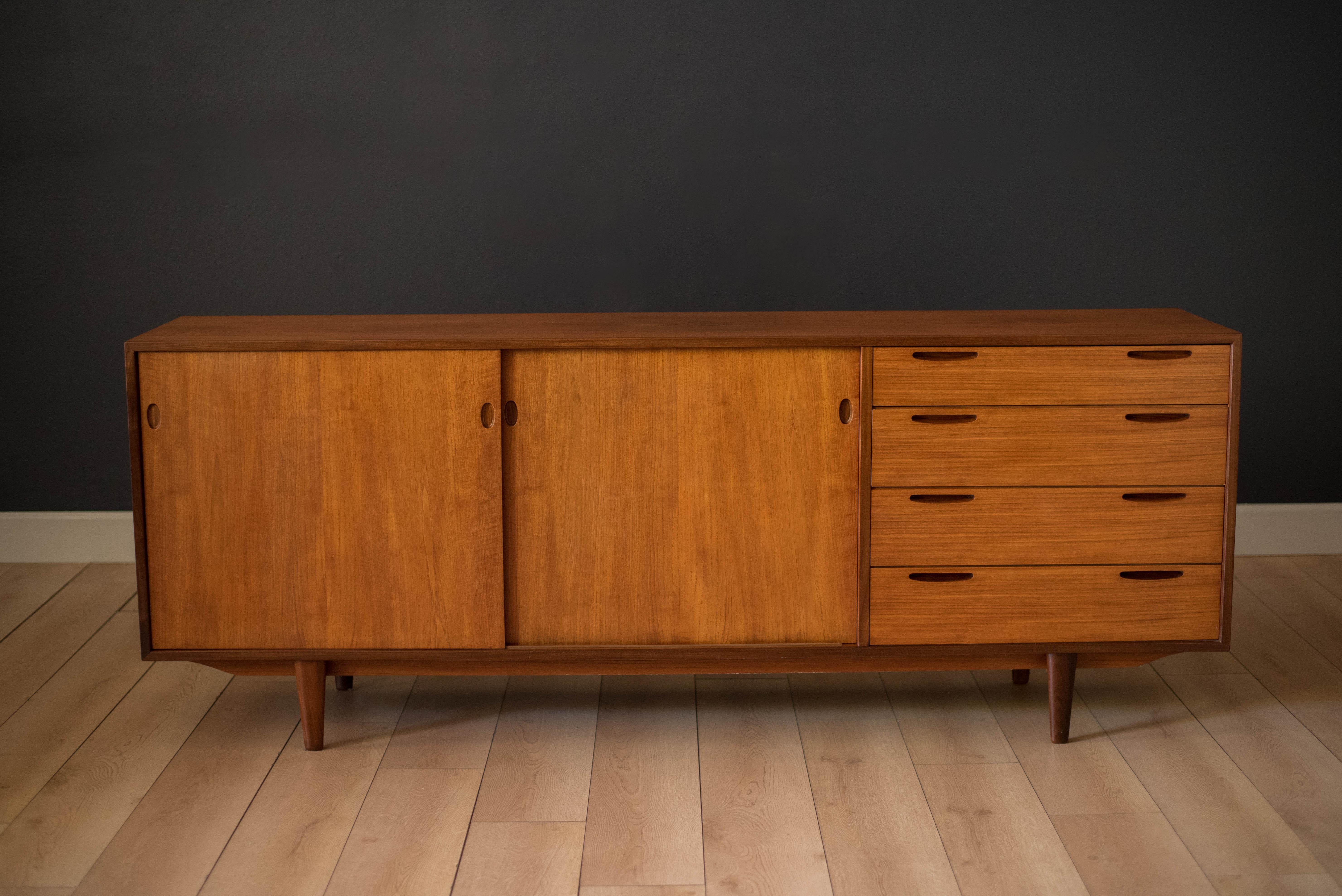 Mid-Century Modern credenza designed by Ib Kofod Larsen for J. Clausen Brande Møbelfabrik. This piece features sliding doors that reveal two interior drawers and open storage with adjustable shelving. Includes four additional drawers with sculpted