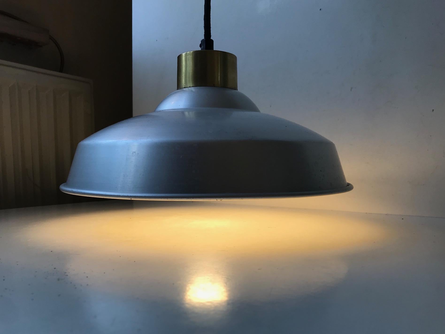 Industrial ceiling light consisting of a raw aluminium main-shade set in a brass top. It was manufactured and designed by NES Belysning in Denmark during the early 1950s. This one came out of an old warehouse in Ribe, Denmark.