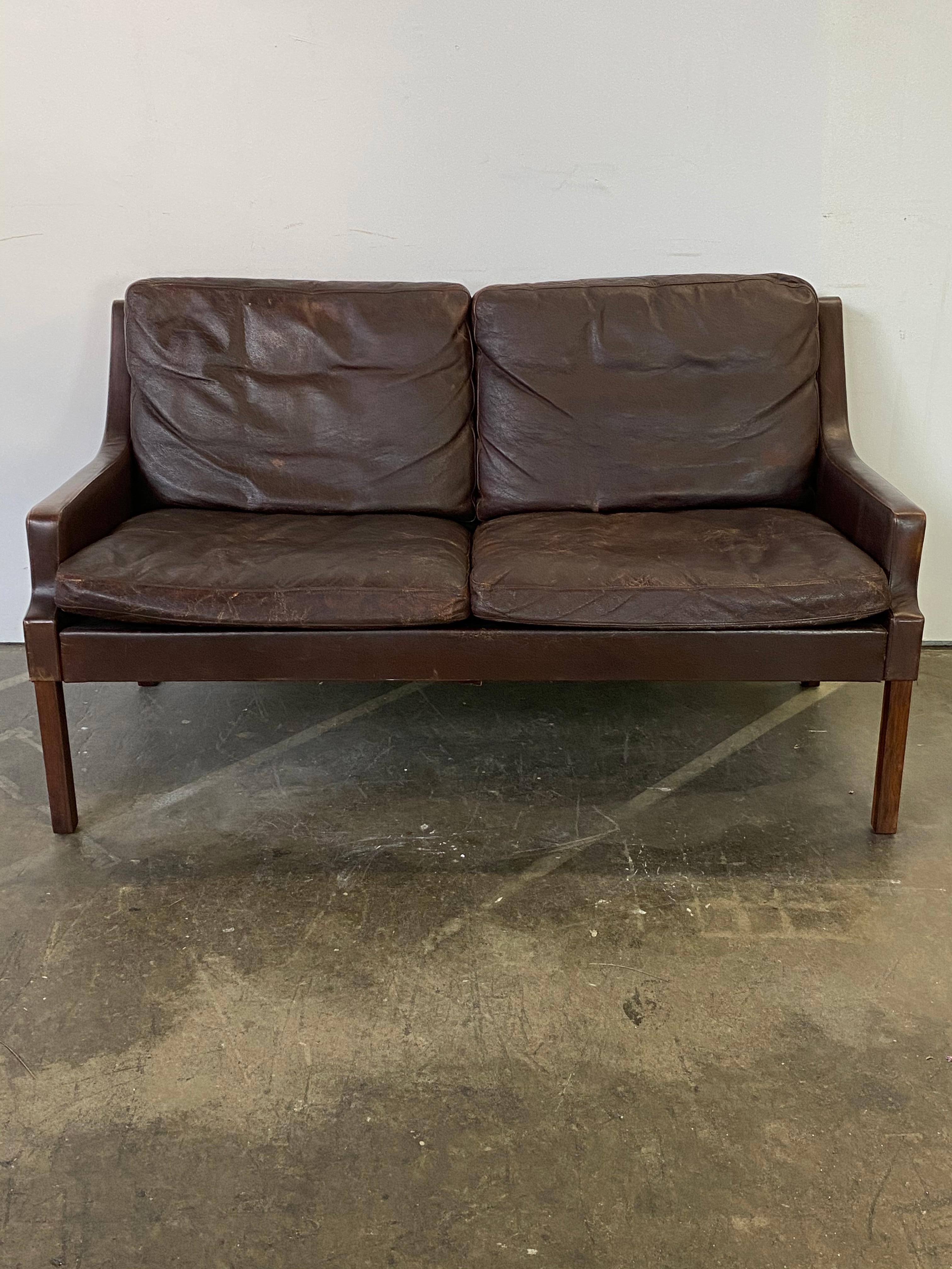Elegant Danish modern loveseat sofa designed by Georg Thams. This piece has aged gracefully and boasts a spectacular Patina on the brown leather cushions, which have been cleaned and conditioned. The 4 rosewood square legs are in good shape with