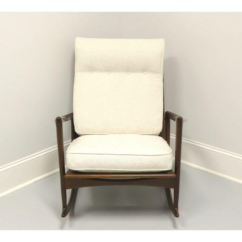 A Mid Century Danish Modern sculpted rocking chair by Ib Kofod-Larsen for Selig. Walnut frame, rounded slats back, cloth seat support straps, neutral cream colored fabric upholstered back & seat cushions, tapered straight legs, and rockers. Made in