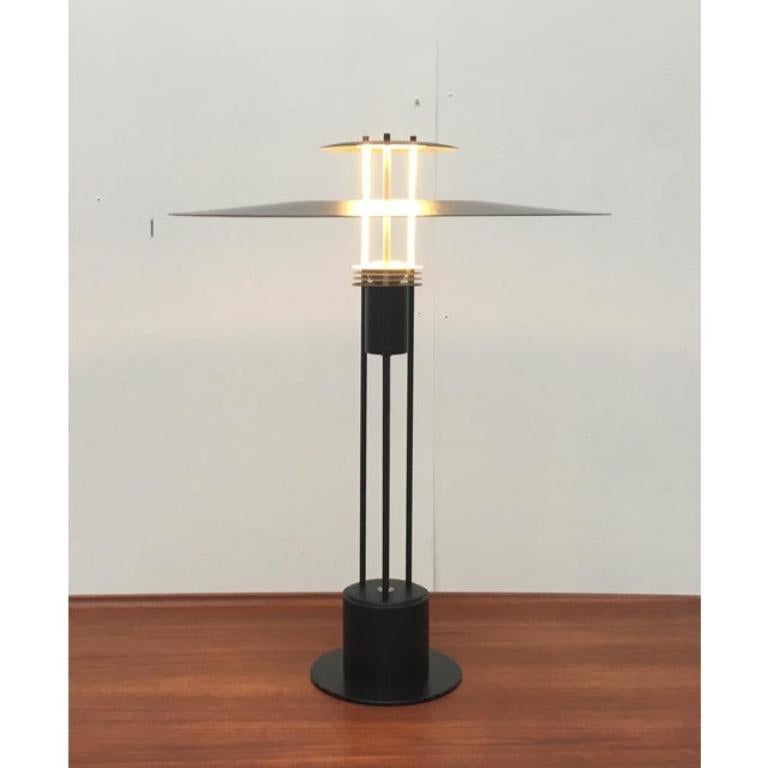 Cette lampe de table Rare provient du fabricant danois Frandsen.

La taille du disque du réflecteur est frappante. Il a un grand diamètre mais une très faible hauteur. Il est à peine visible de profil, ce qui confère à ce design une élégance