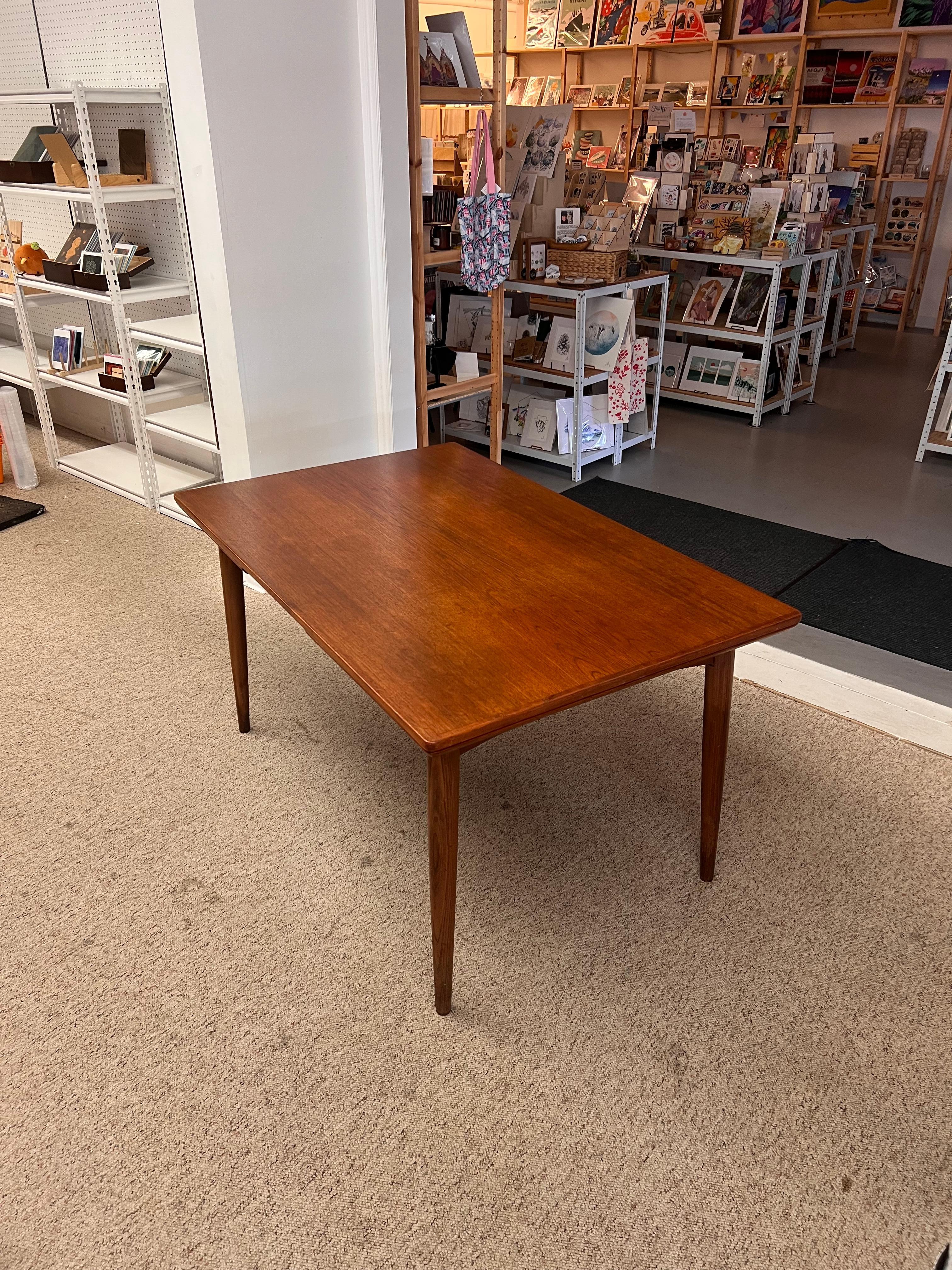 Cette table de salle à manger danoise moderne du milieu du siècle présente un design épuré et minimaliste typique de l'époque. La table est fabriquée dans un bois aux tons chauds, probablement du teck ou un autre bois dur, dont le grain naturel est