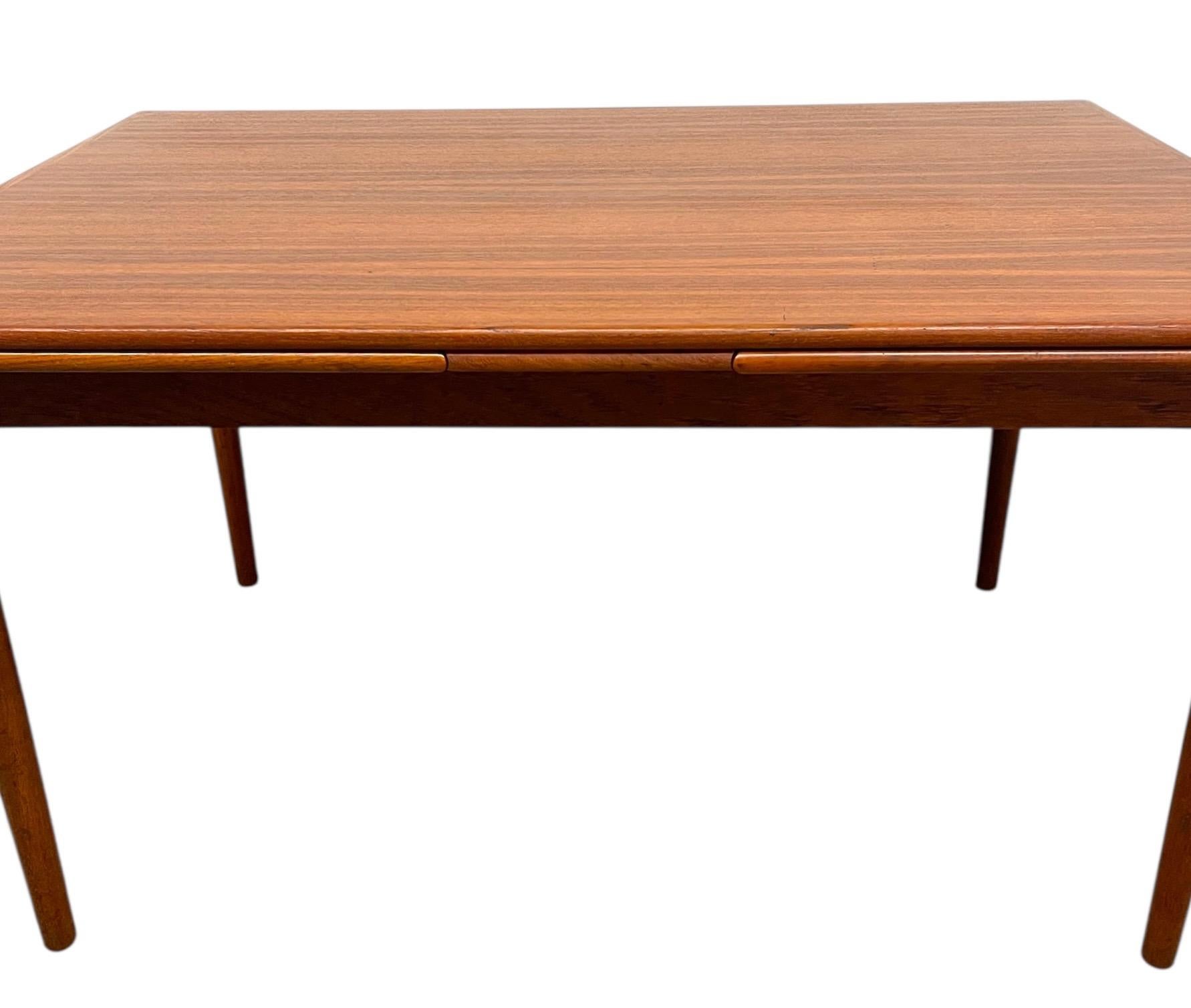 Le plateau de table rectangulaire présente un motif de grain de teck joliment rayé avec des bords doucement arrondis, soutenus par des pieds minces et effilés qui soulignent le profil élégant et léger de la table.
L'une des principales