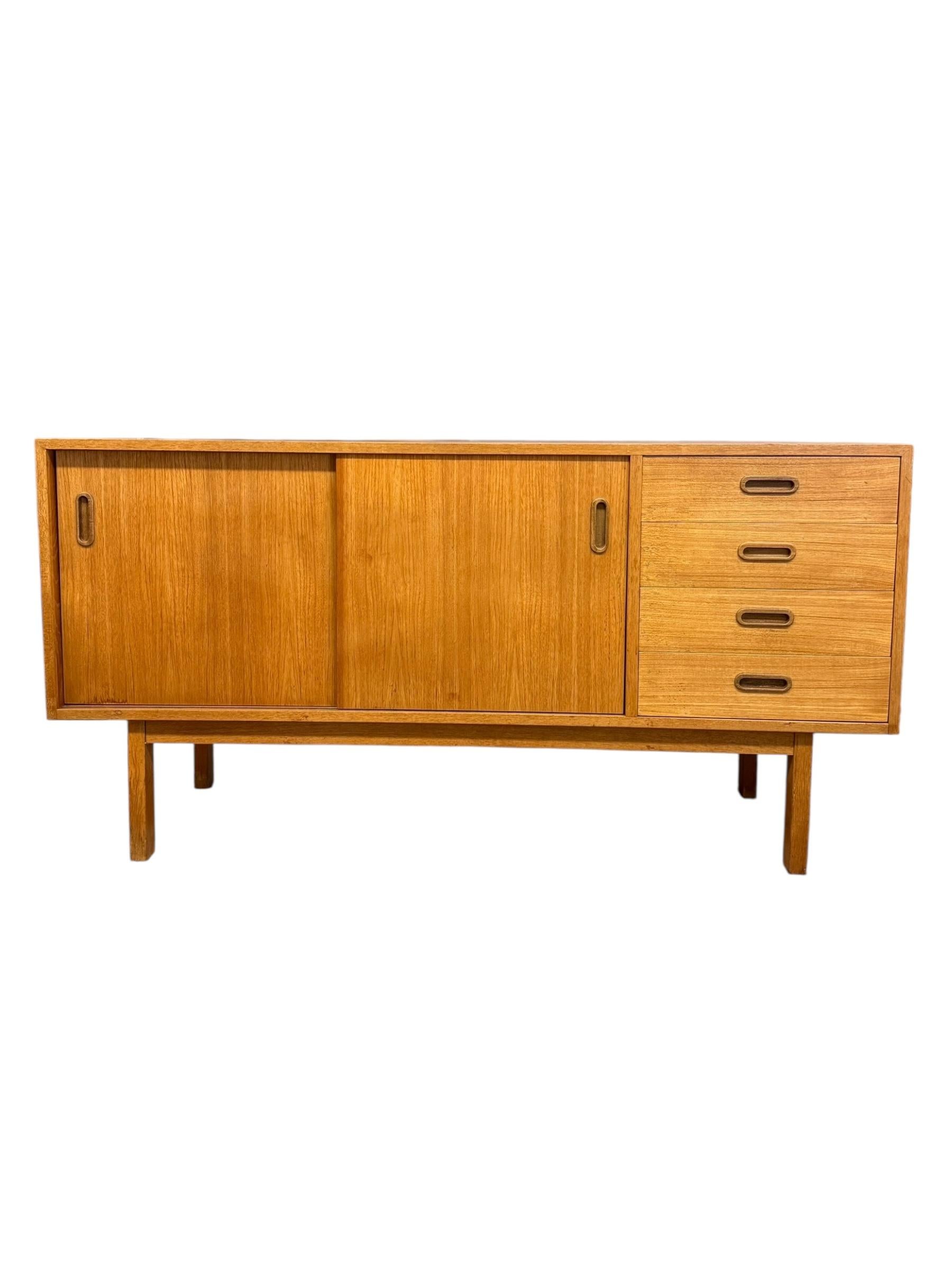 Cette crédence moderne importée du milieu du siècle présente une structure rectangulaire en bois avec une finition chaude en chêne clair. Il se compose d'un plateau plat, de deux portes coulissantes sur le côté gauche révélant un intérieur ouvert