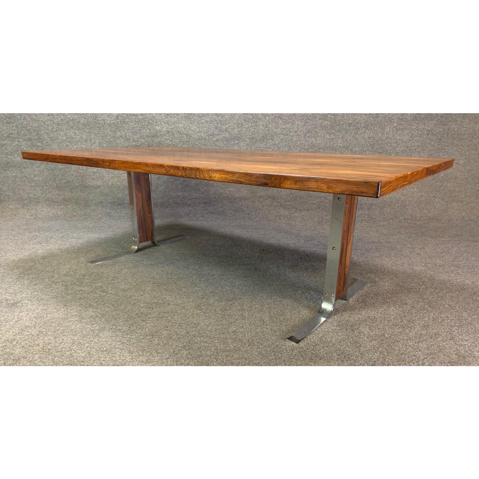 Voici une grande table basse moderne scandinave en bois de rose et accent chromé fabriquée au Danemark dans les années 1970.
Cette table basse, dans son état d'origine, présente un grand plateau avec un grain de bois vibrant et deux pieds