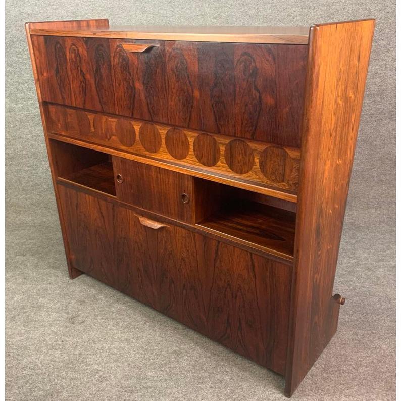 Here is the rosewood version of the famous cocktail bar model SK661 designed by Johannes Andersen and manufactured by Skaaning & Søn in Denmark in the 1960s.
This amazing conversation piece, with its amazing vibrant rosewood grain detail, features