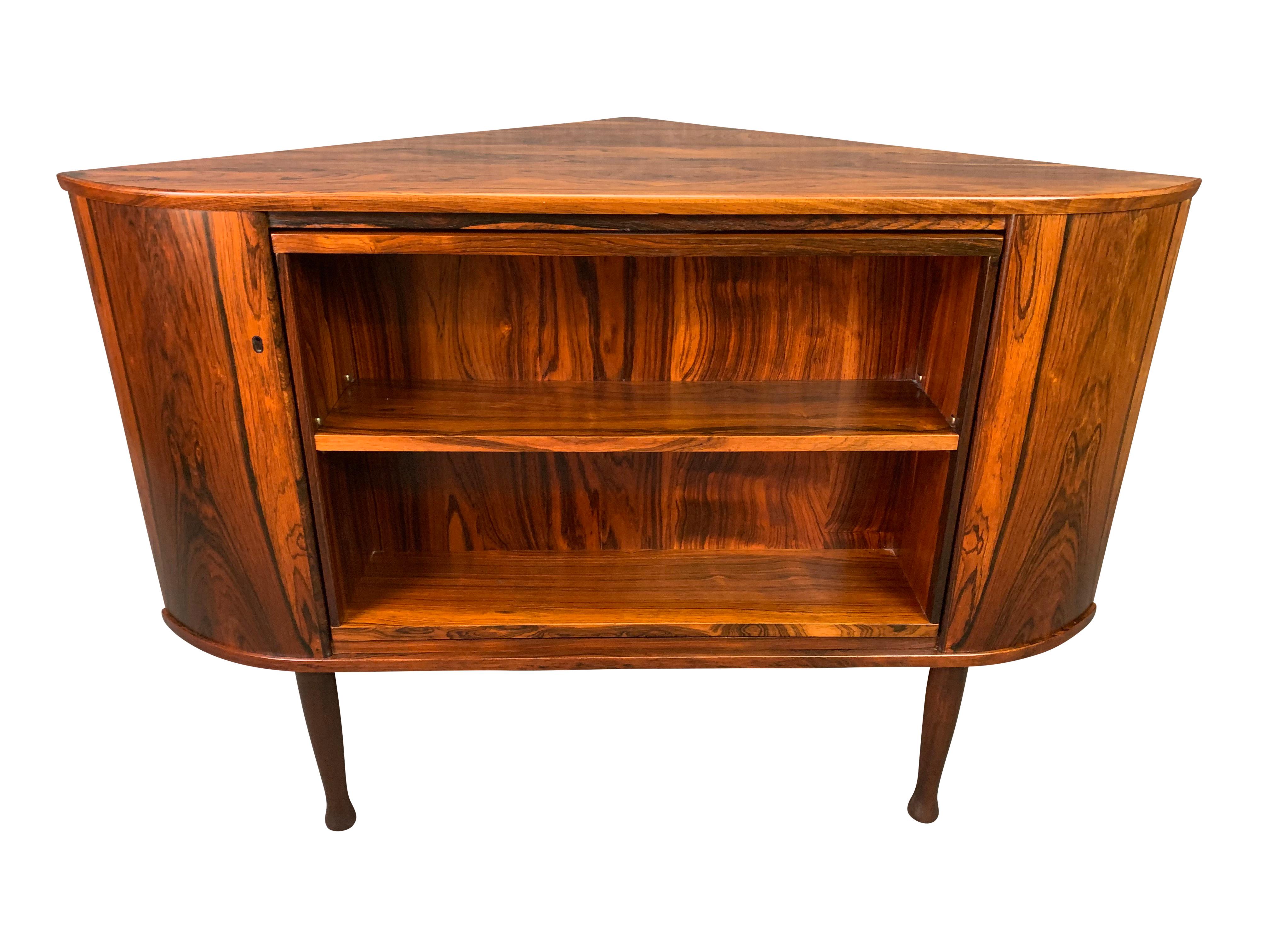 Here is an exceptional 1960s Scandinavian Modern corner cabinet in rosewood featuring a rotating inside with a dry bar and display case sides. This special piece features a vibrant grain and four sculpted tapered legs.
The bookcase side of the unit