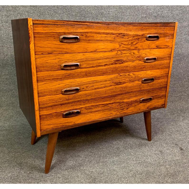Here is a beautiful Scandinavian Modern chest of drawers in rosewood from the 1960s recently imported from Denmark to California.
This lovely dresser seats on four slanted tapered legs and features a vibrant wood grain and four dove tail built