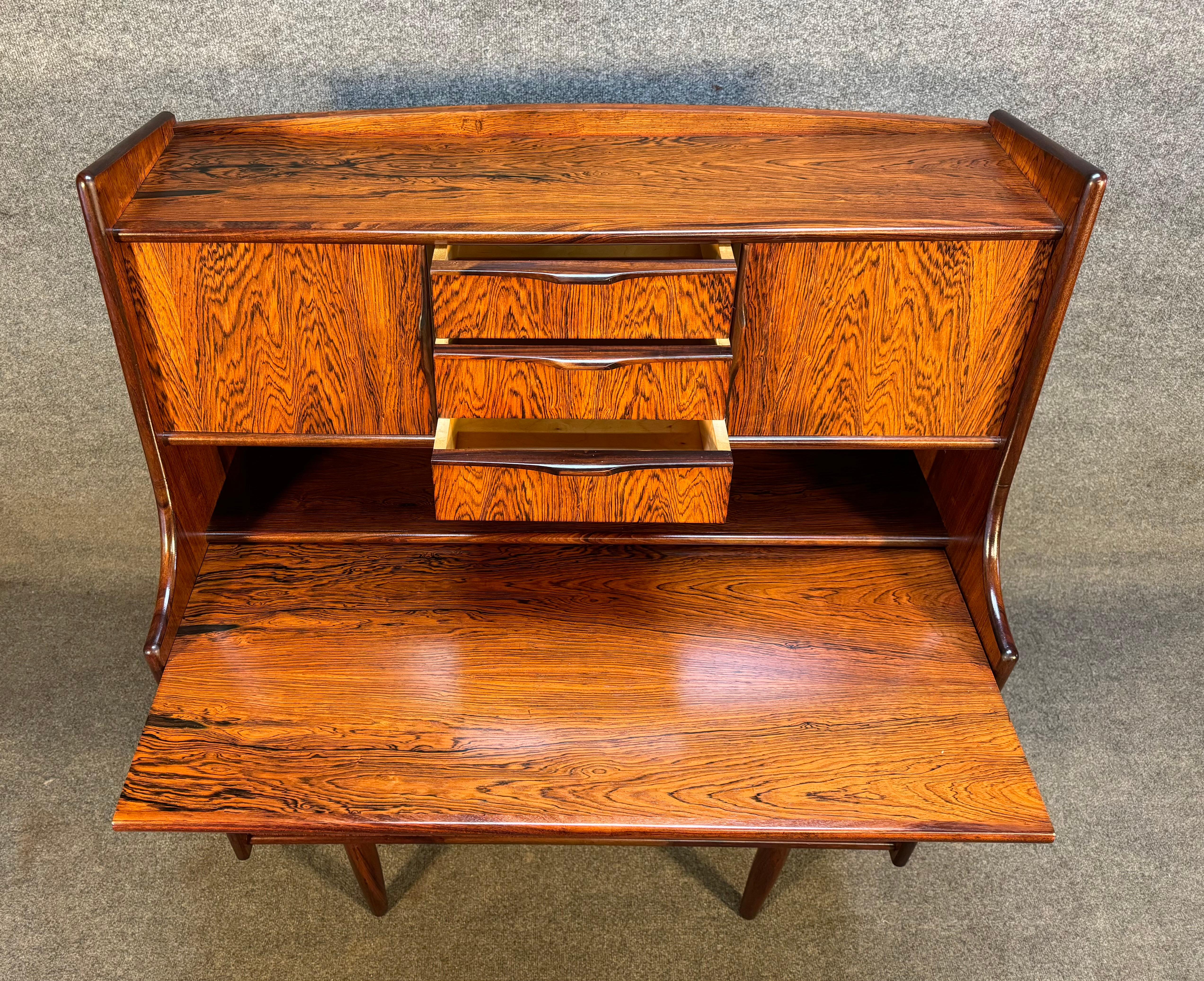 Here is a beautiful scandinavian modern secretary desk in rosewood manufactured in Denmark in the 1960's.
This exquisite case piece, recently imported from Europe to California before its refinishing, features a vibrant wood grain, a central bank of