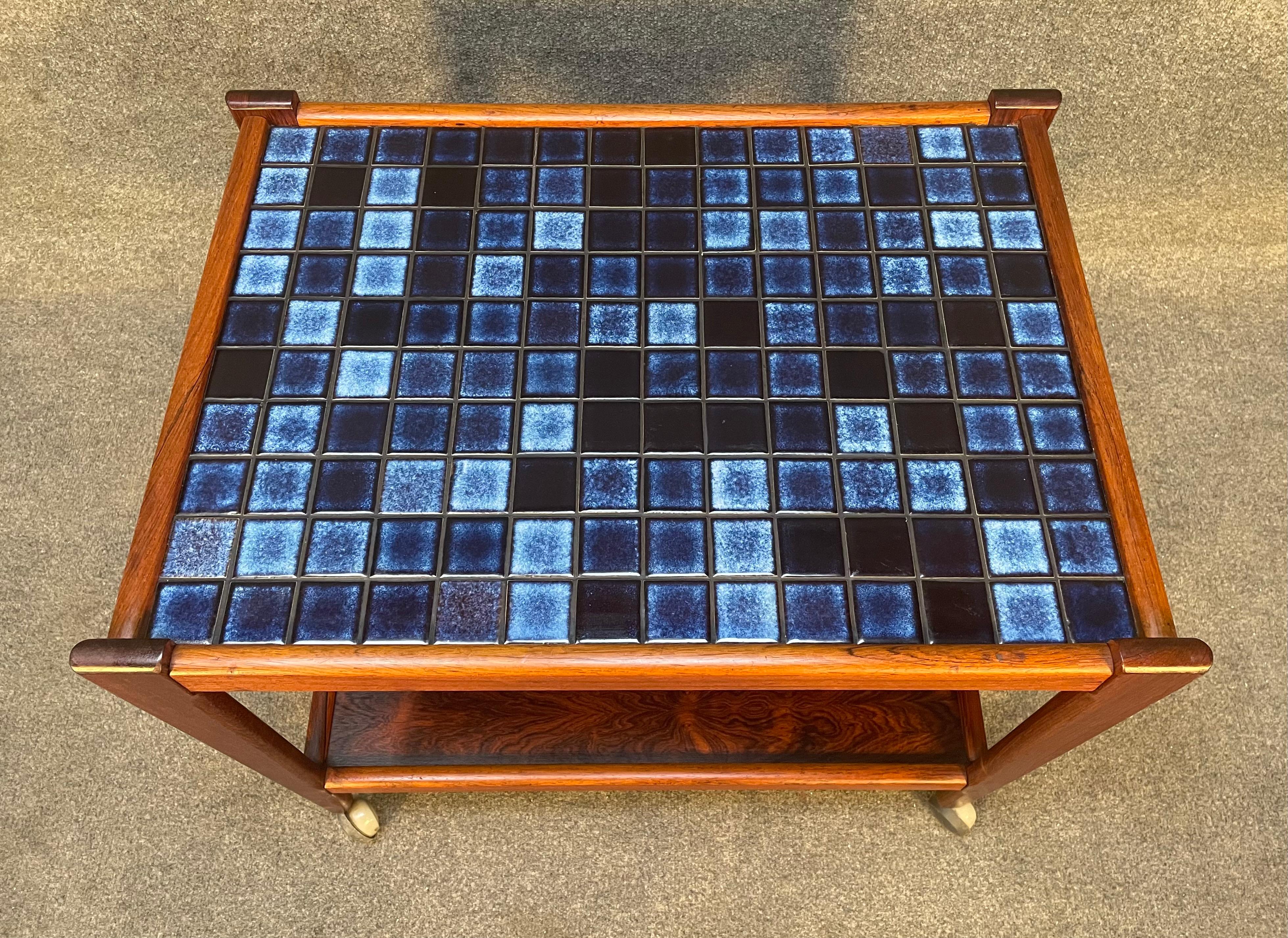 Here is a beautiful scandinavian modern bar cart in Brazilian rosewood manufactured in Denmark in the 1960's.
This exquisite piece, recently imported from Europe to California, features a top inlayed with blue tiles of different shades, a lower