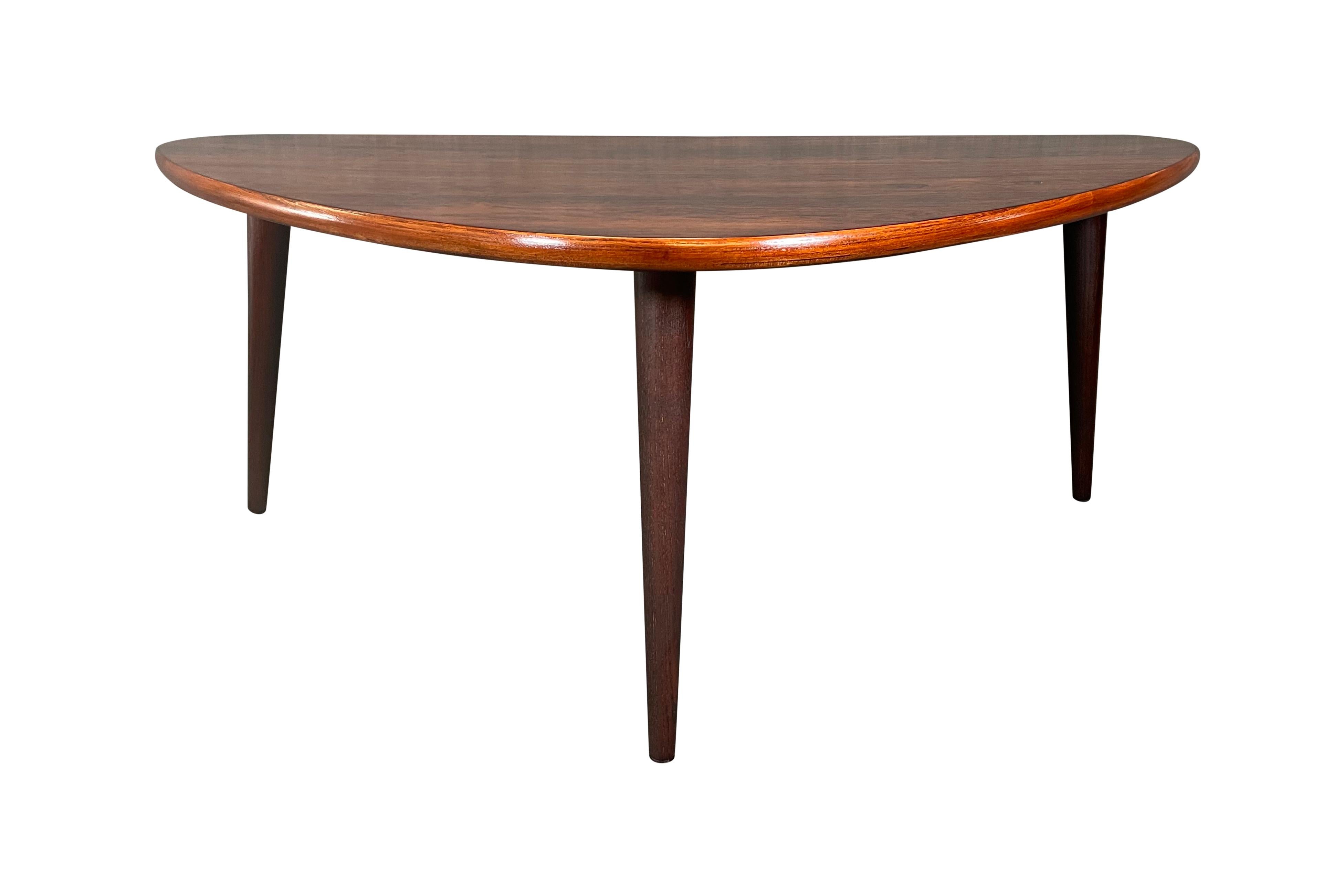 Here is a beautiful scandinavian modern coffee table in rosewood manufactured in Denmark in the 1960's.
This lovely table, recently imported from Europe to California before its refinishing, features a vibrant wood grain on its top and three