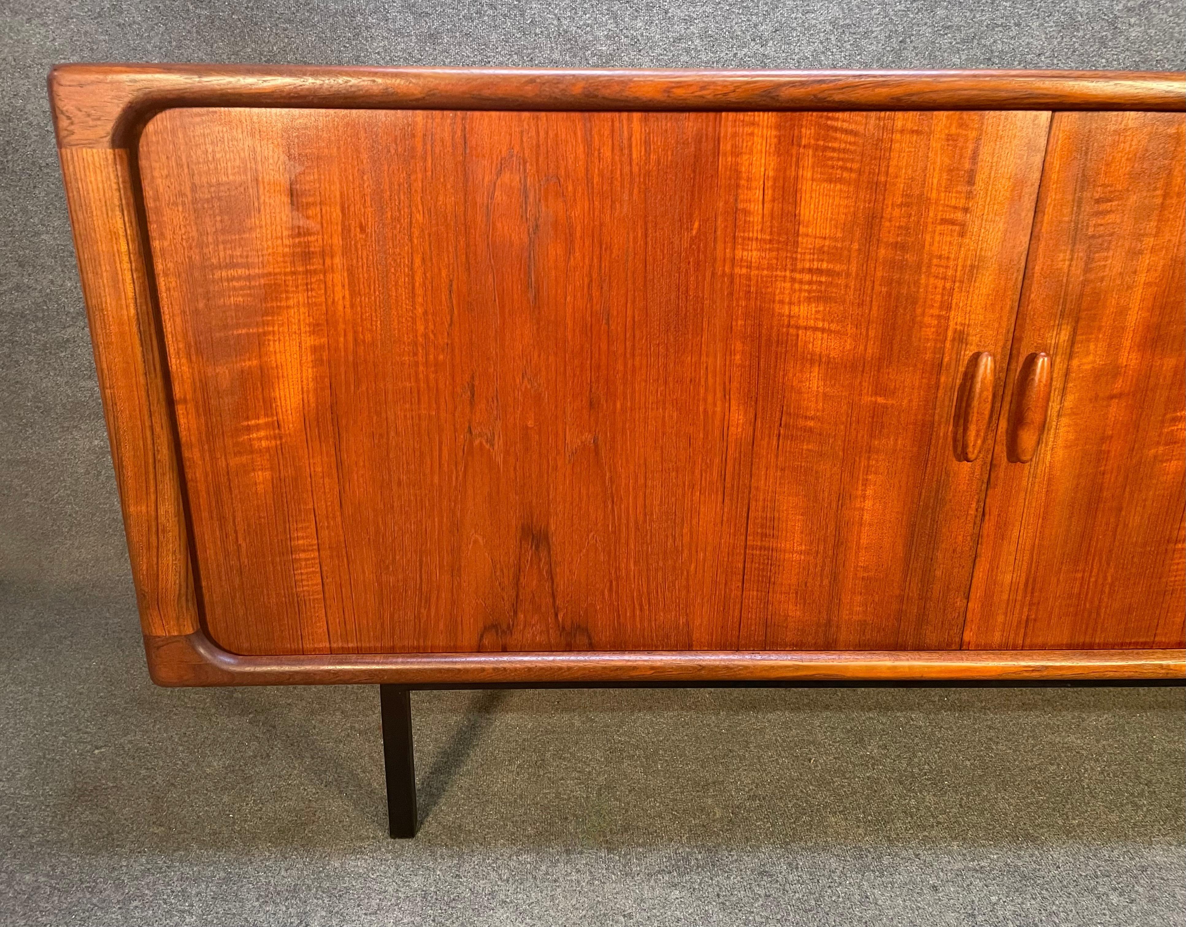 Here is a beautiful scandinavian modern teak sideboard manufactured by Dyrlund in the 1970's.
This exquisite credenza, recently imported from Europe to California before its refinishing, features a vibrant wood grain, two large smooth rolling