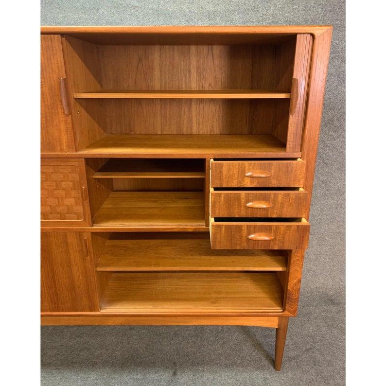 Here is a stunning Scandinavian Modern highboard in teak wood manufactured by Uldum Mobelfabrik in Denmark in the 1960's.
This case good, recently imported from Copenhagen to California, features vibrant teak wood grain, two smooth rolling tambour