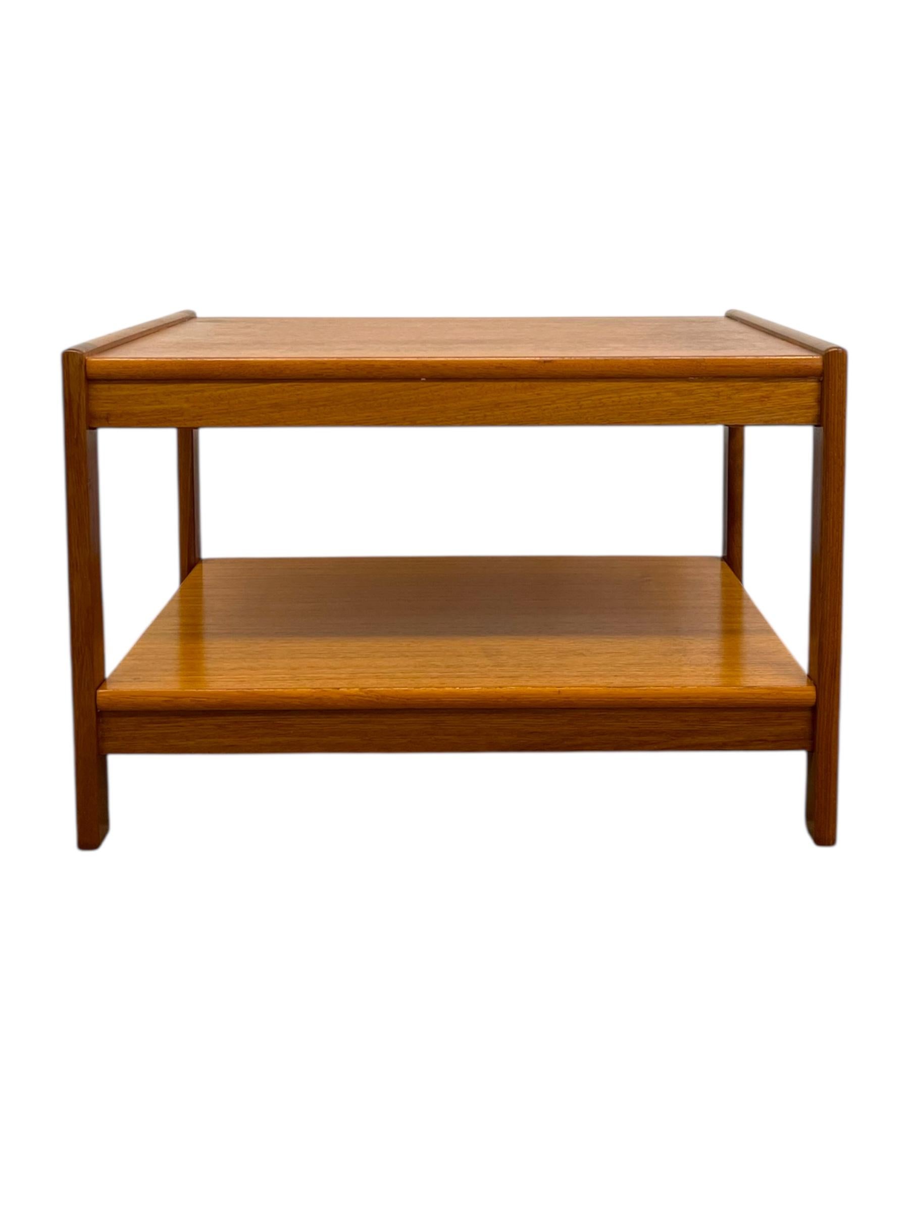  Esta mesa auxiliar vintage danesa de teca moderna de mediados de siglo presenta un diseño de líneas limpias y funcionales característico de la artesanía escandinava. Construida en teca y chapa de teca, la mesa presenta cálidos tonos dorados y un