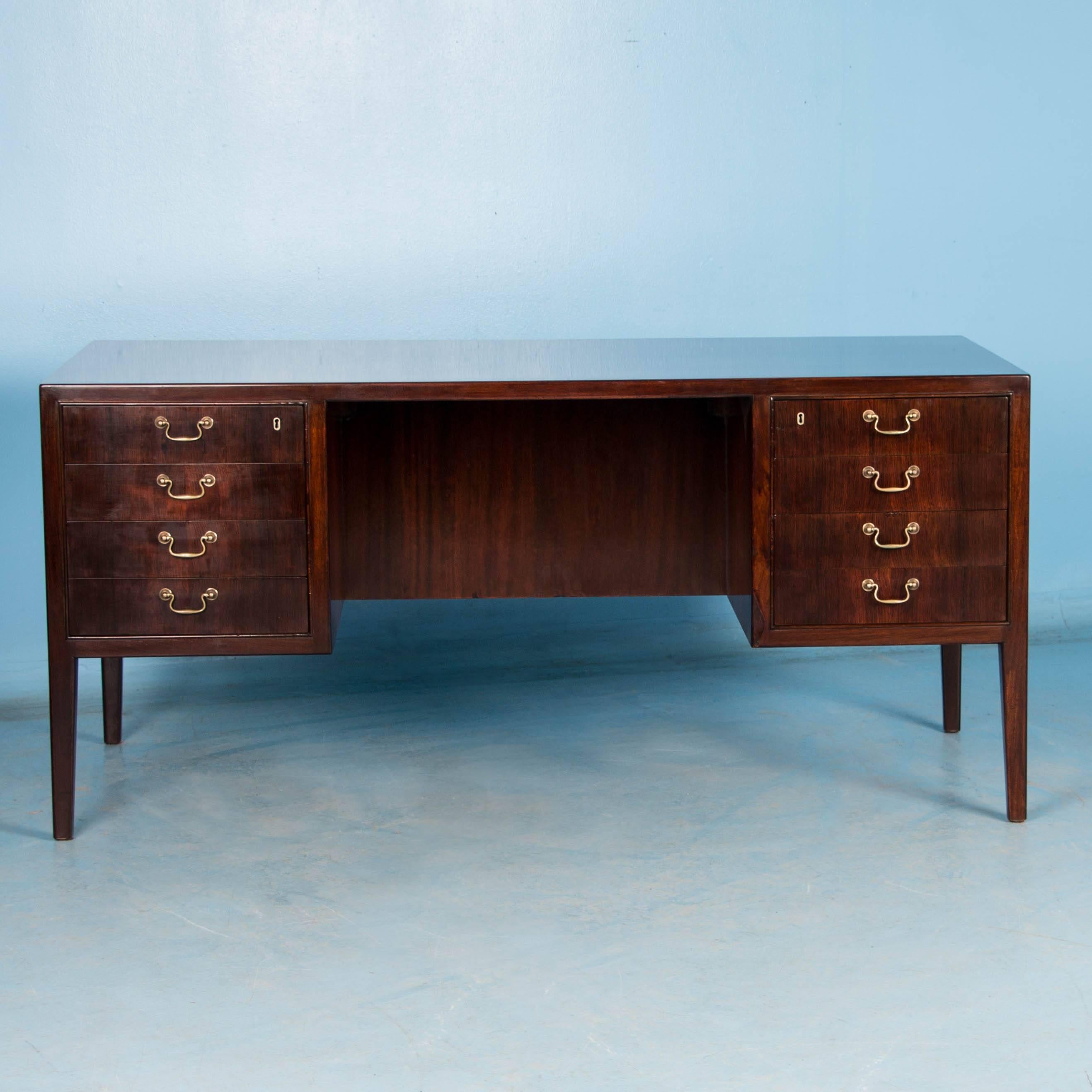 The bookmatched rosewood desk top, sides and drawer fronts are stunning and in exceptional condition. The rich, deep color of the rosewood compliments the mid-century style in this desk with locking drawers and original brass pulls. The tapered legs