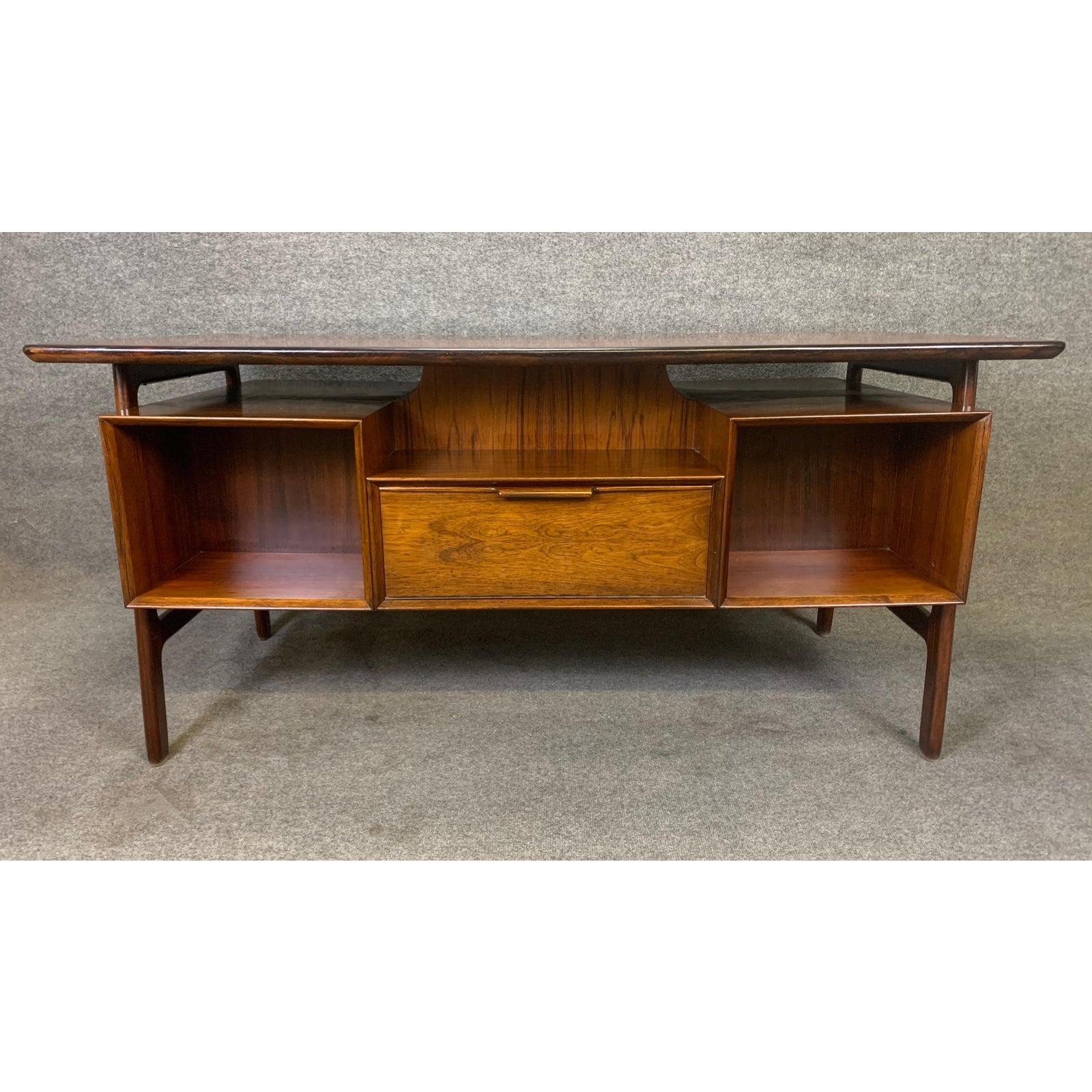 Here is the iconic model 75 desk in Brazilian rosewood designed by Gunni Omann and manufactured by Omann Jun Møbelfabrik.
This stunning 1960s Scandinavian Modern desk features a sculpted leg frame supporting seamlessly two floating banks of three