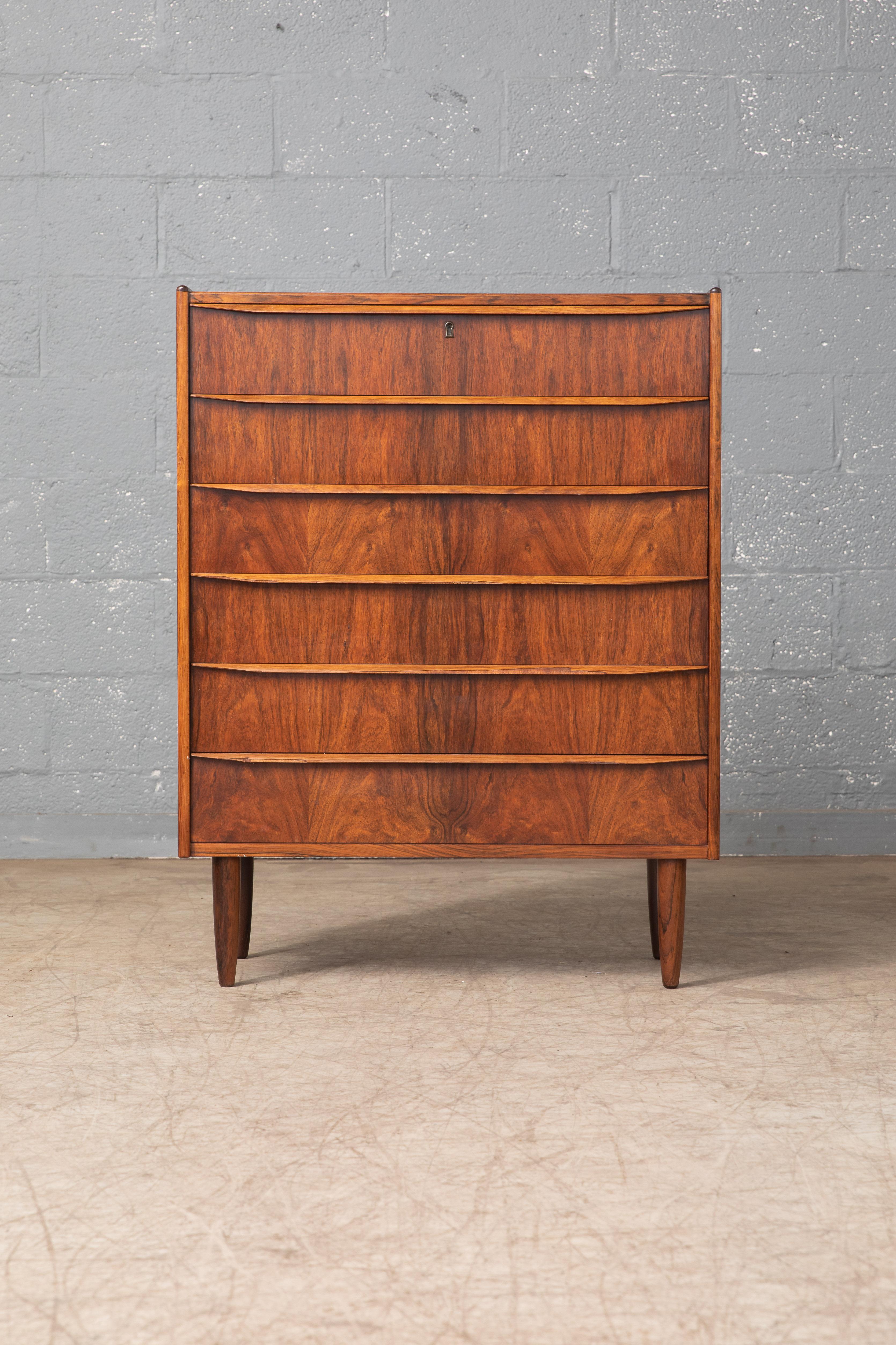 Exquisite 1960s rosewood chest of drawers with six large drawers in bookmatched rosewood veneer. High quality craftmanship with solid raised edges and carved drawer pulls. Unmarked. Very good condition with just a few pices of missing veneer on a