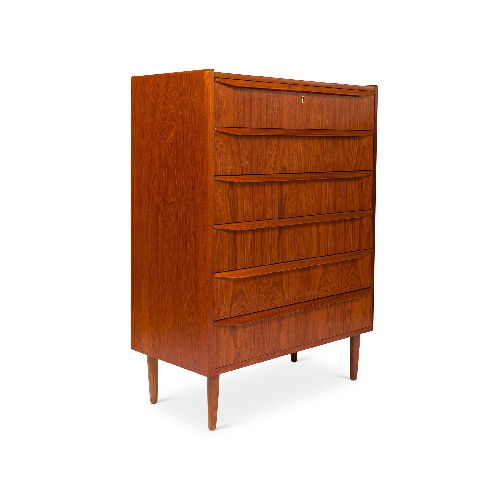 A stunning 1960s vintage Danish mid-century six-drawer teak tallboy dresser stands as an emblem of timeless design. The chest of drawers exhibits a mesmerizing teak grain, complemented by elongated sculpted drawer pulls. Its embodiment of the Danish