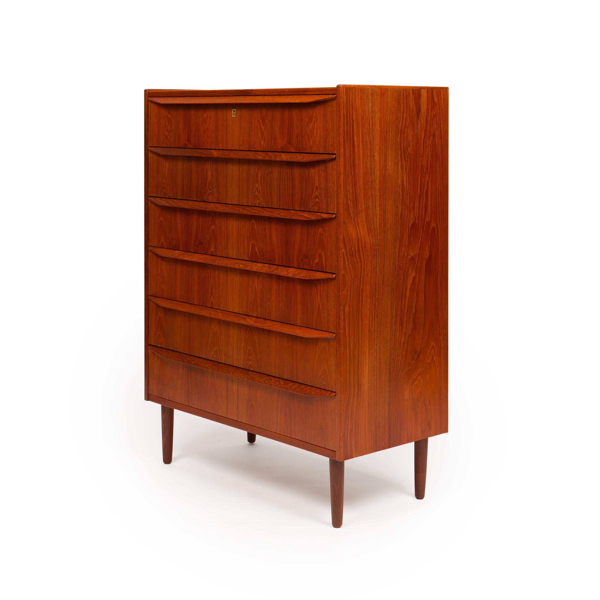 Questa splendida cassettiera danese Mid-Century in teak del 1960 è un pezzo di artigianato senza tempo. Caratterizzata da squisite venature del legno e da cassetti in teak intagliati a mano, questa cassettiera alta offre sei cassetti spaziosi con un