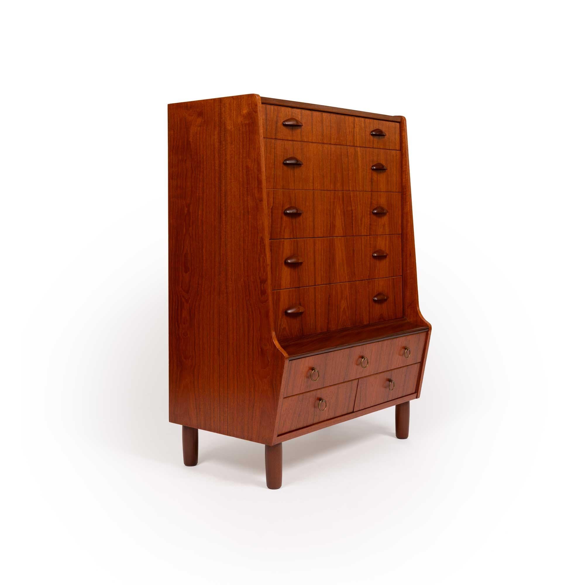 This beautifully crafted vintage Danish mid-century teak dresser was made in Denmark in the 1960s. This dresser has eight drawers, five with carved teak drawer pulls and three with circular brass pulls. This dresser has exquisite teak wood-grain