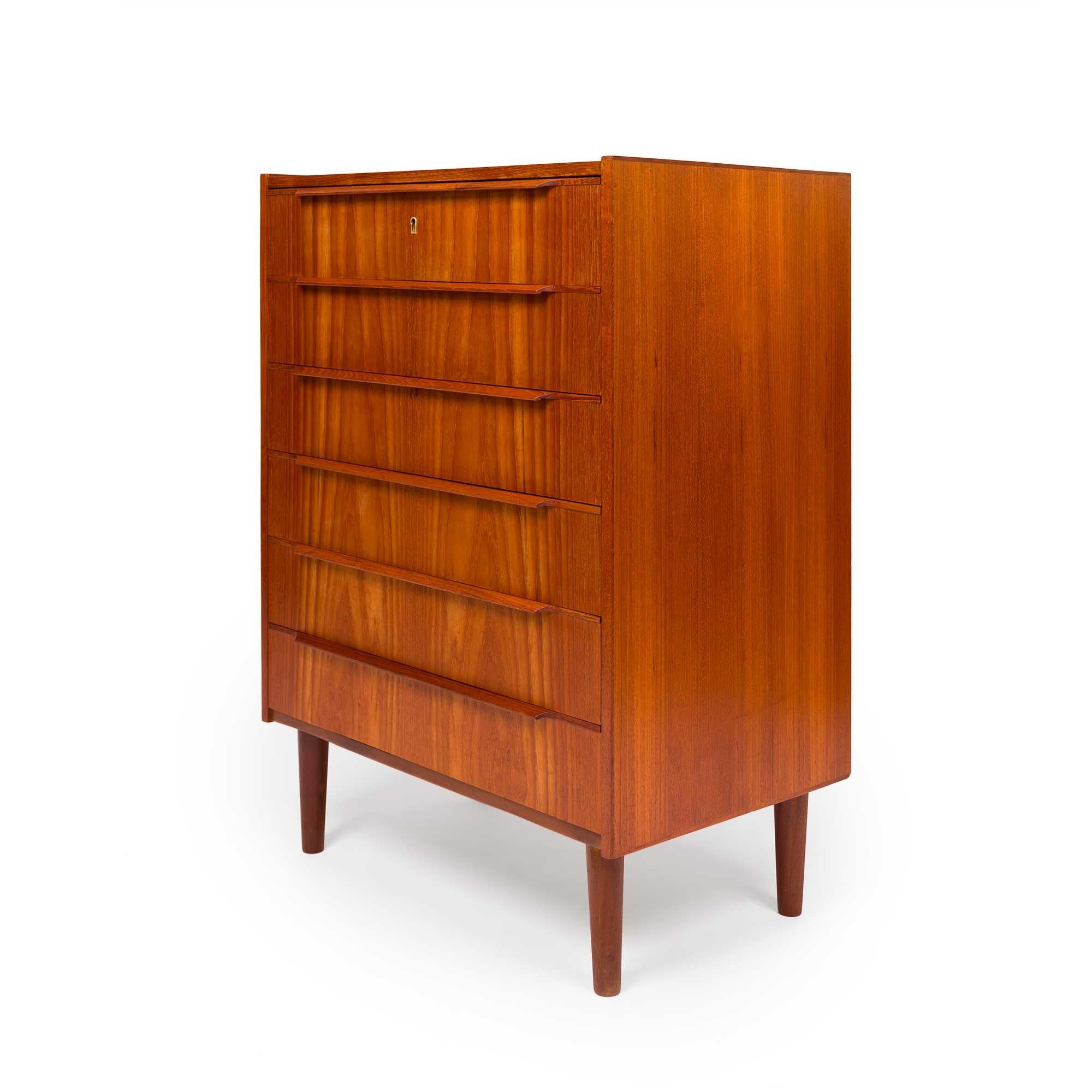 This Danish tallboy chest of drawers embodies the essence of Mid-Century design. Its six drawers, adorned with sculptured wooden handles and seamless dovetail joins, effortlessly combine functionality with elegance. The natural teak grain adorns its