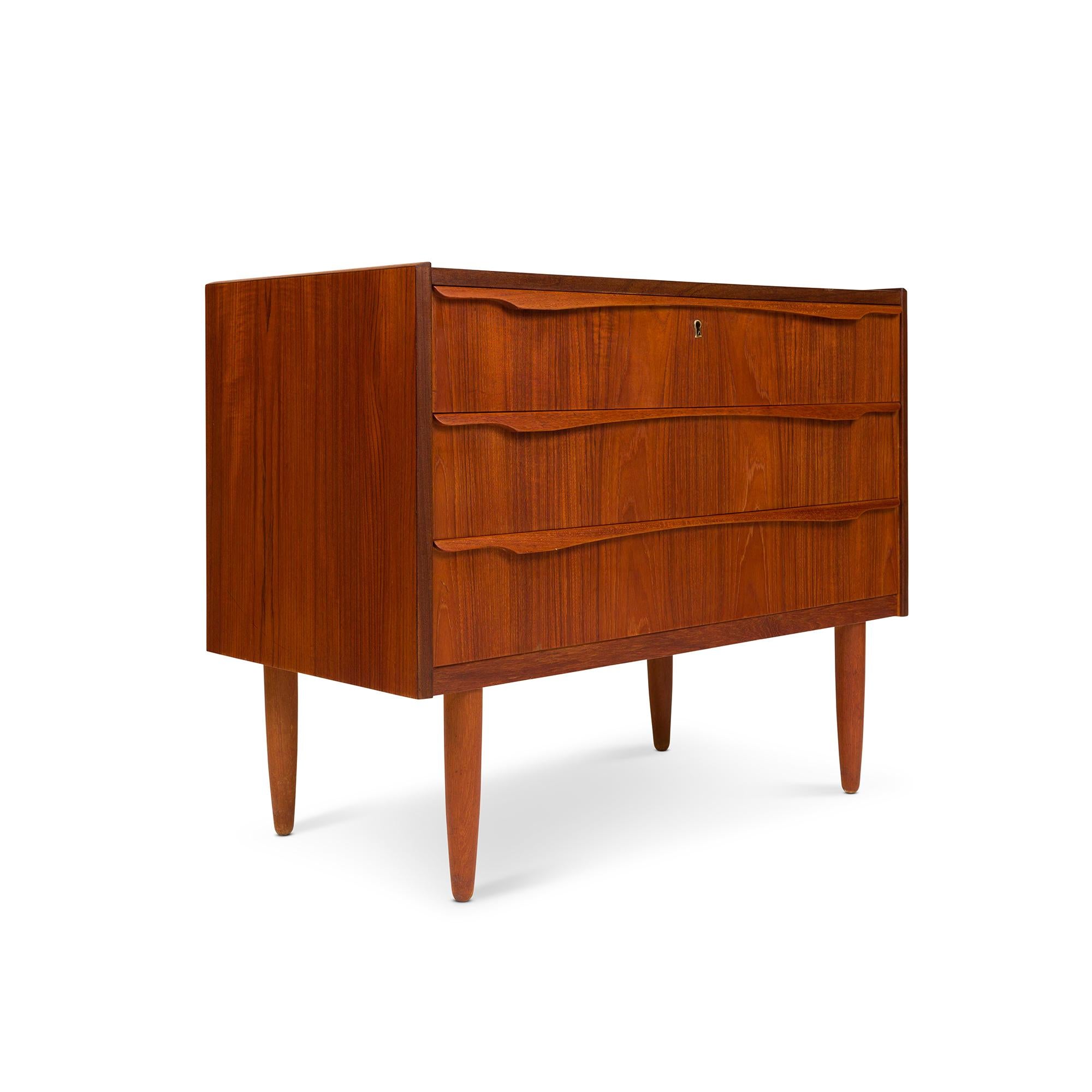 Exuding timeless elegance, this vintage Danish mid-century modern lowboy dresser boasts exquisite teak wood grain that captivates the eye. Its allure lies in the three impeccably crafted drawers adorned with intricately carved drawer pulls, all in