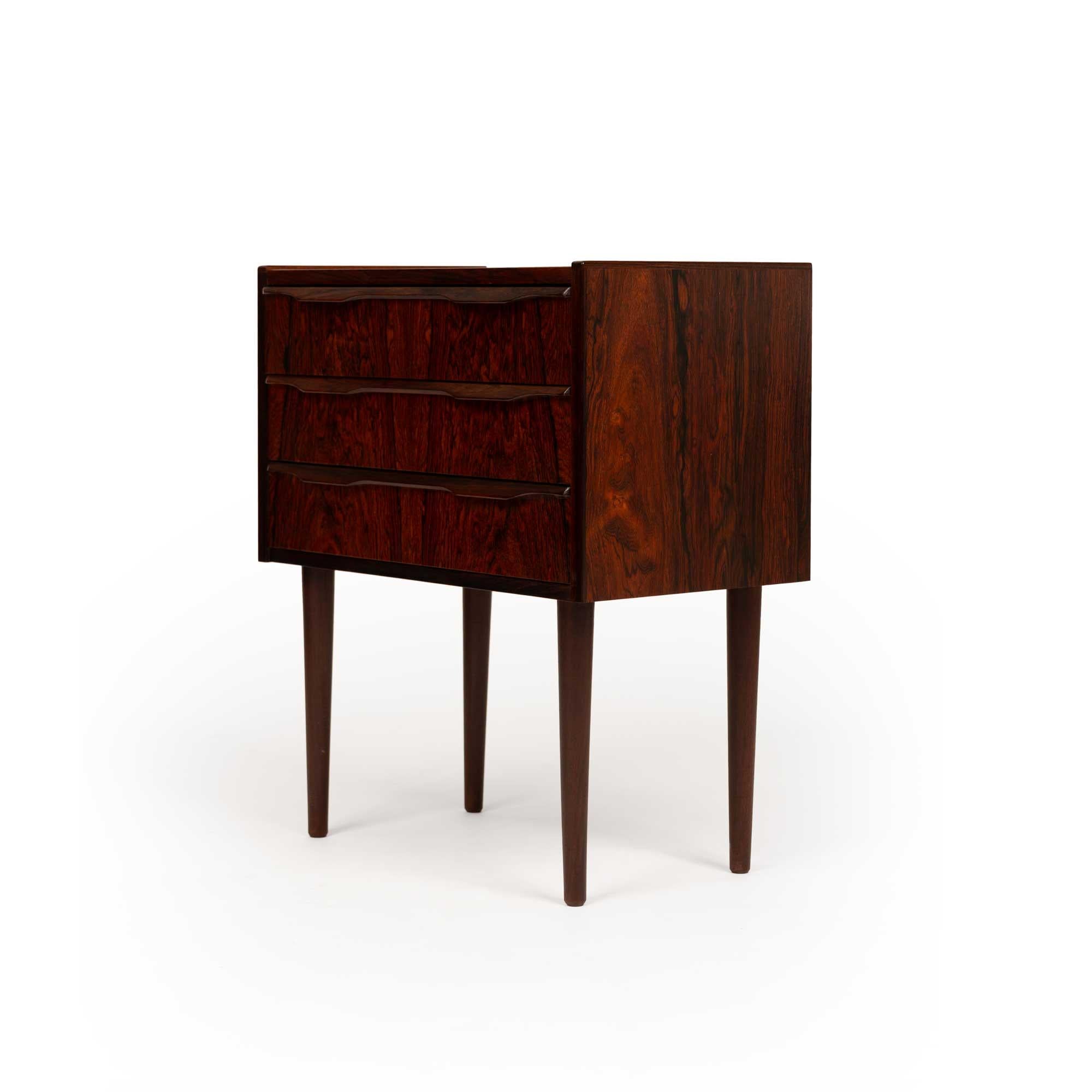 Cette superbe commode danoise vintage à trois tiroirs, de style The Modern Scandinavian, est un exemple parfait du design scandinave intemporel. Entièrement fabriqué en bois de rose richement grainé, il témoigne de la qualité exceptionnelle et du