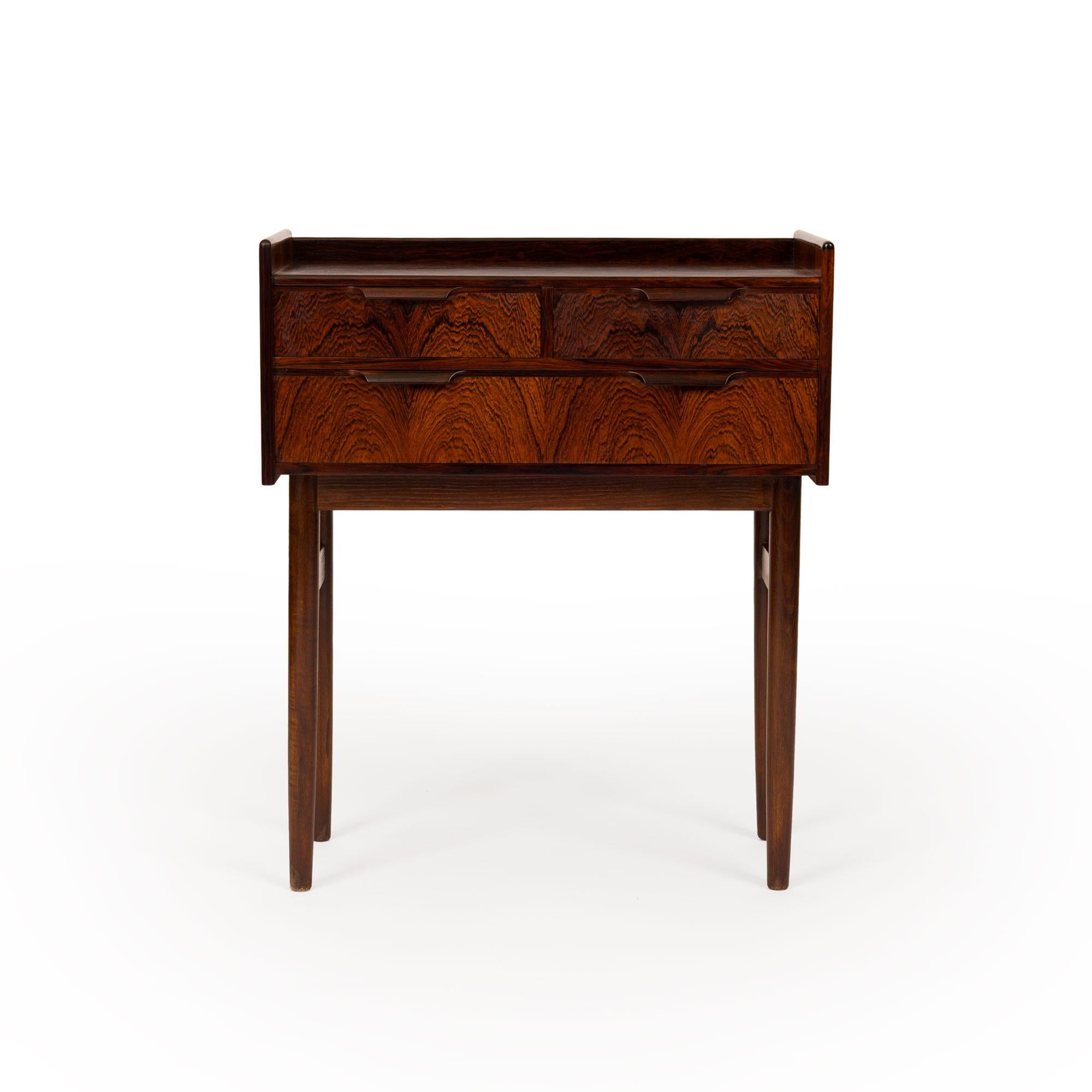 Cette exquise commode danoise moderne du milieu du siècle à trois tiroirs est une représentation frappante du style scandinave classique. Construite dans les années 1960 et réalisée en bois de rose richement figuré, cette pièce reflète les matériaux