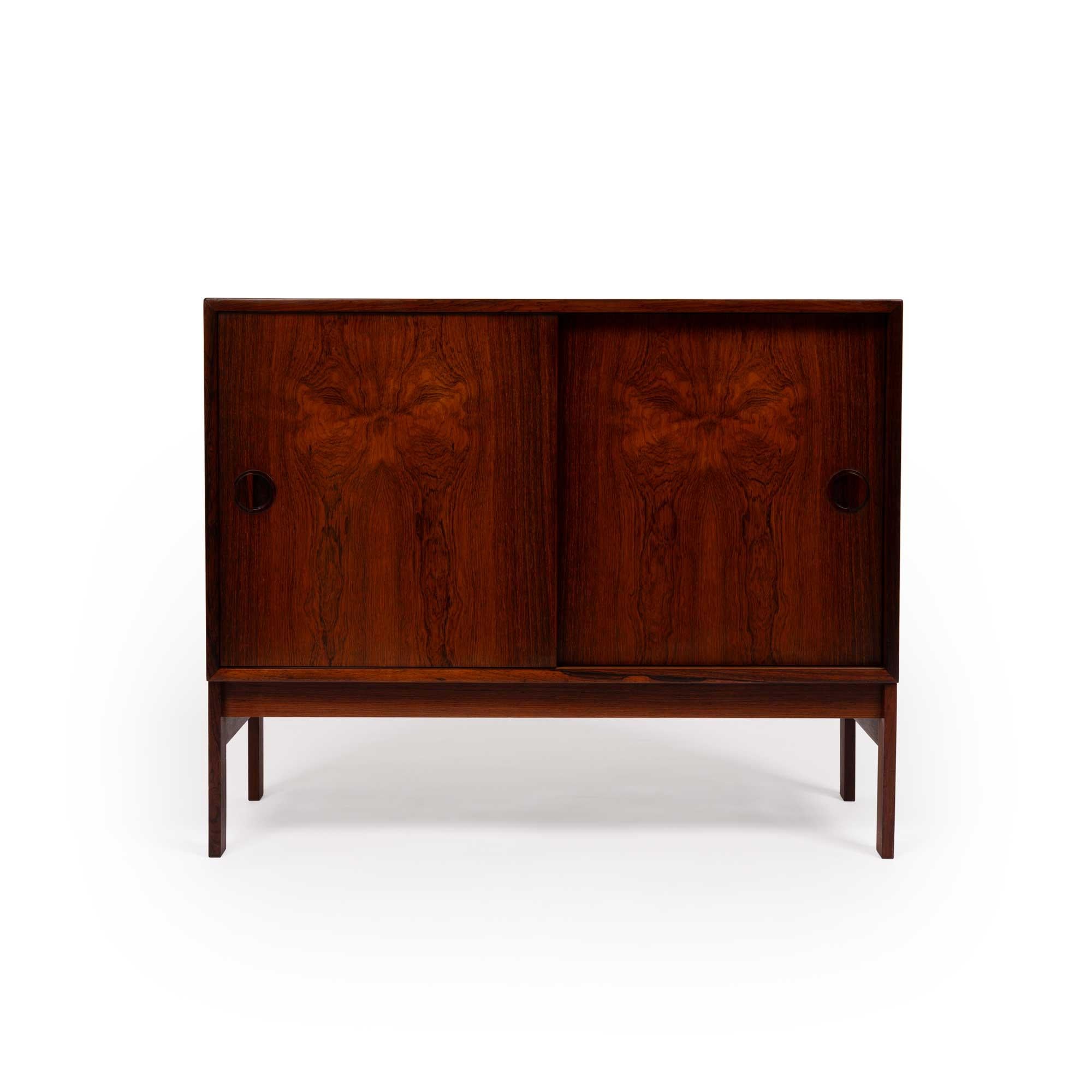 This vintage Danish Modern rosewood cabinet, compact yet functional, is a timeless piece that combines elegance and practicality. Featuring two separate compartments, each equipped with an adjustable shelf, it offers versatile storage options while