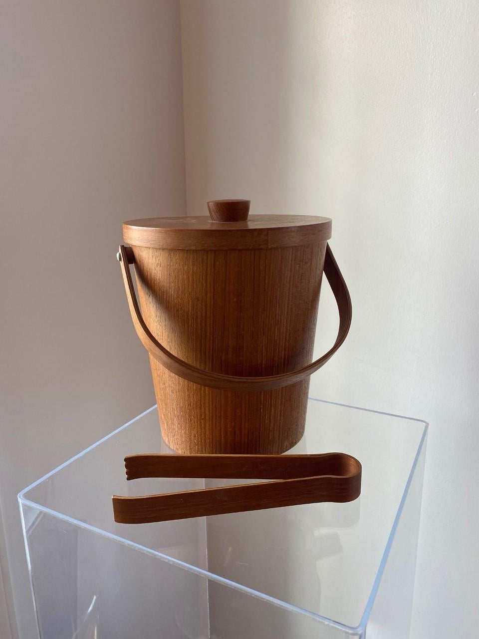 Unique and beautifully crafted Danish midcentury teak ice bucket. This piece has minimal, clean lines while enveloped in the grain of teak with the insert of aluminum. The piece comes with original set of ice tongs. Linear in shape but rich in