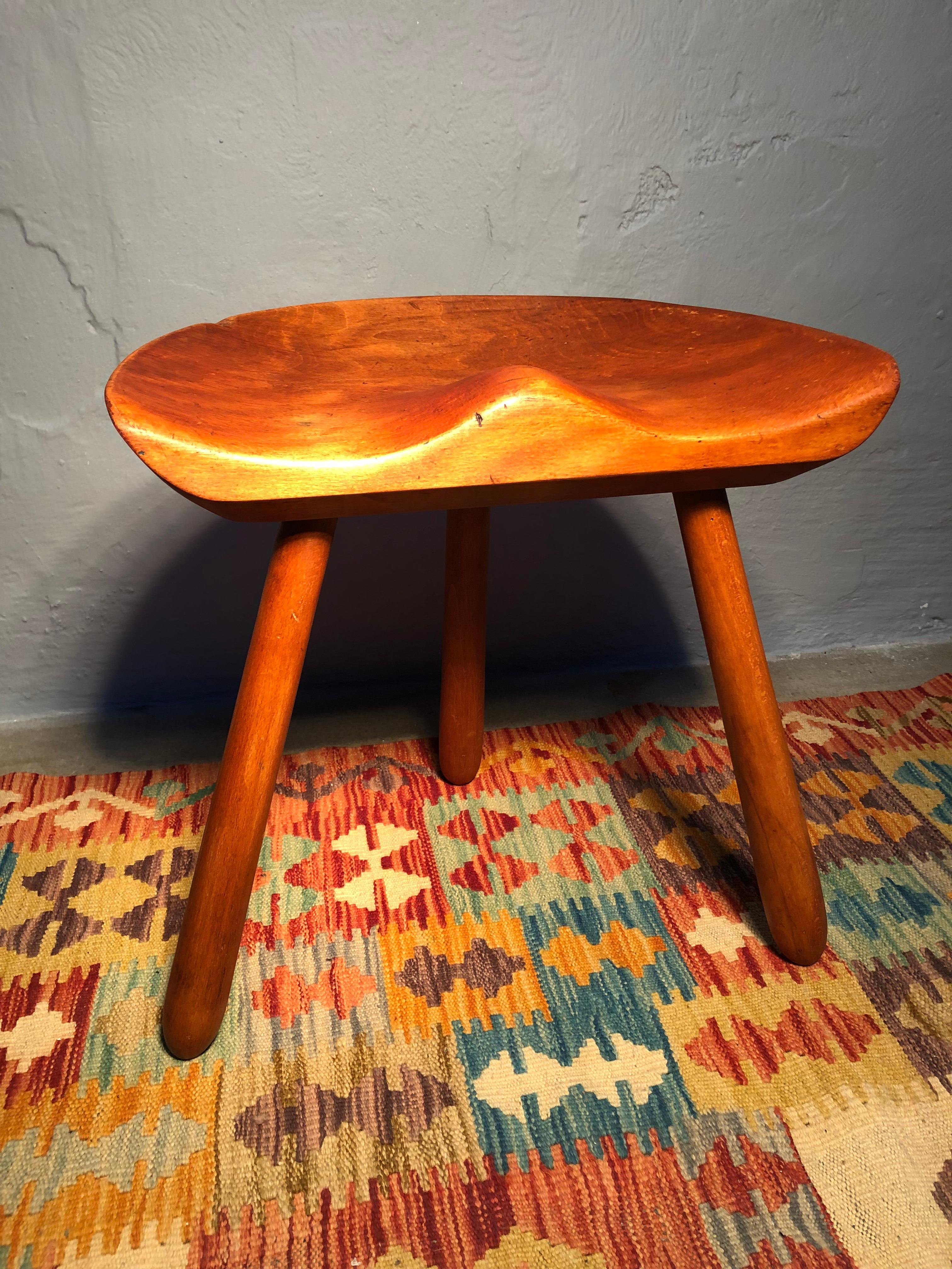 A mid Century milking Stool in beech wood. 
With a sculptural and simplistic Scandinavian design and with a carved seat and turned legs. 
The stool has been sanded and waxed. 
With age related wear and patina from years of use.