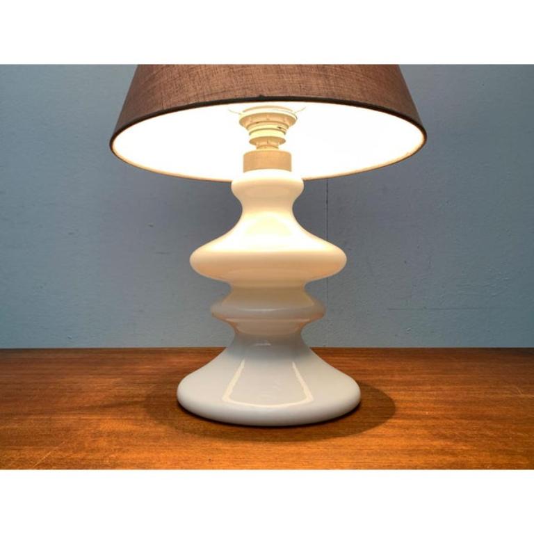 Élégante lampe de table du fabricant danois Holmegaard d'après un projet de Per Lütken des années 1970.

Un design classique avec un langage de conception traditionnel. Cette lampe à poser convainc par son pied ornemental en verre opale blanc. Les