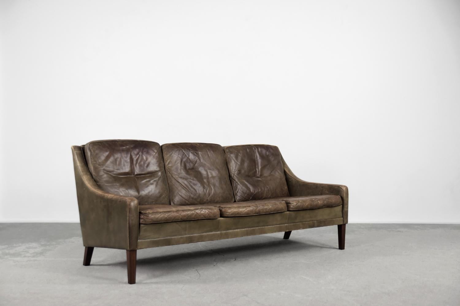 Dieses dreisitzige Mid-Century Modern Vintage-Sofa wurde in den 1950er Jahren in Dänemark hergestellt. Das Sofa ist mit Naturleder in einer braunen und erdigen Farbe gepolstert. Das Leder hat eine schöne originale Patina. Er hat drei lose Sitz- und