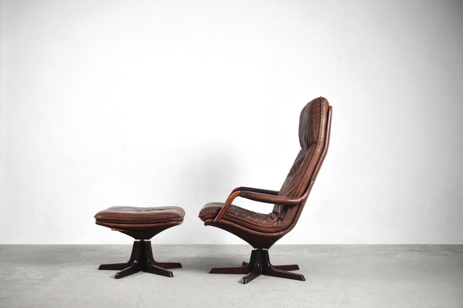 Ce fauteuil et cet ottoman vintage ont été produits au Danemark par Berg Furniture dans les années 1970. Ceux-ci étaient revêtus de cuir brun à la patine naturelle et magnifique. La base et les accoudoirs sont en bois. La chaise et le repose-pieds