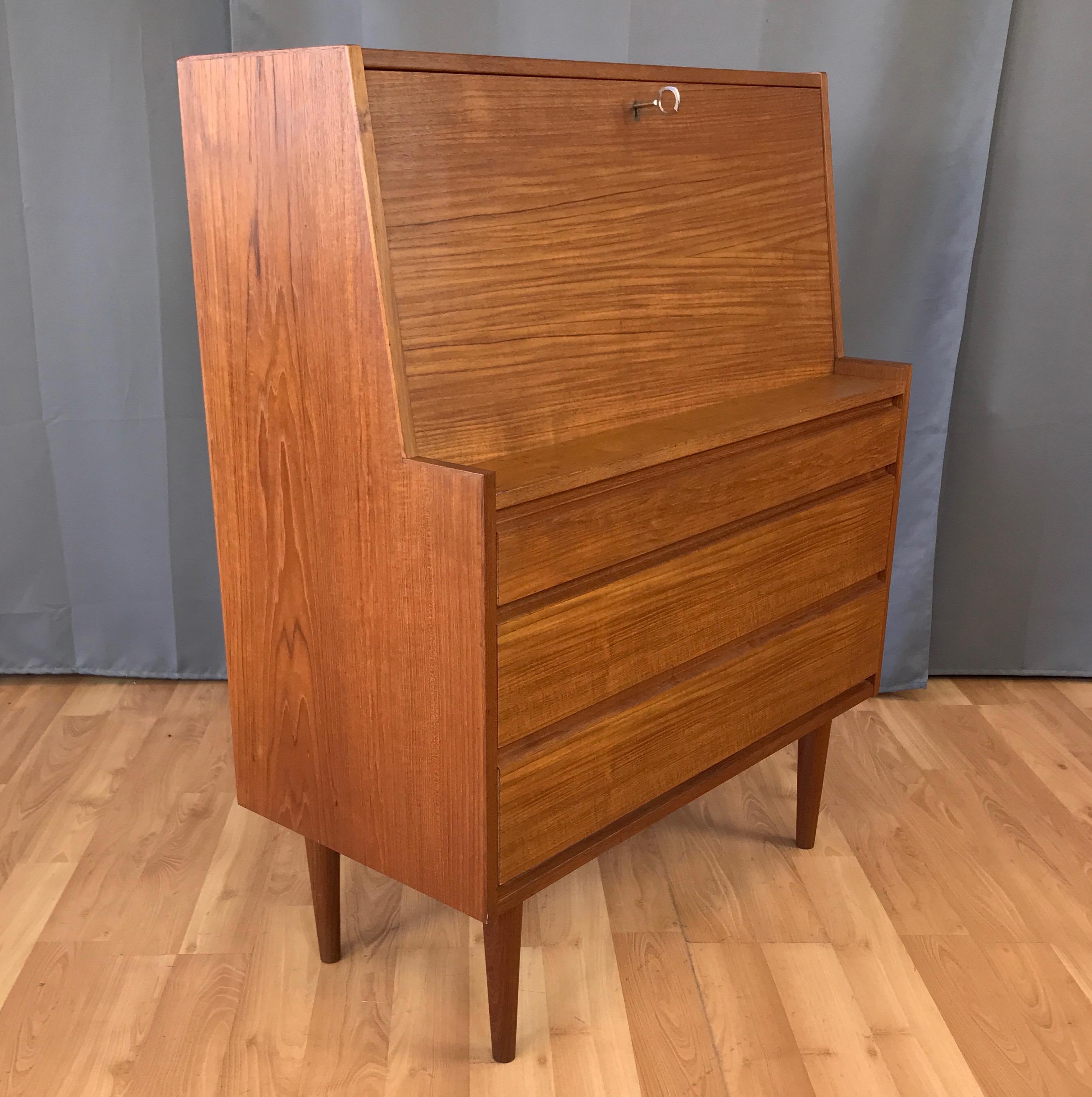 A Danish Modern lockable teak secretary, circa late 1960s to early 1970s.

Compact design with clean lines and beautiful bookmatched teak. Three wide drawers with dovetail joinery and nicely finished interiors. Lockable drop-down front with