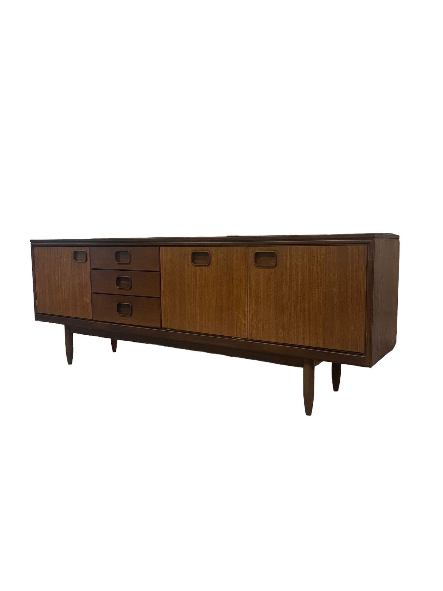 Possibly Teak Sideboard with Three Drawers and a Fall Front , Flanked by Two Cupboard Doors, Enclosing Shelves, Finished Back , Raised on Tapered Legs. Top Drawer is Felted with Dividers as Shown. English Designer. Imported From UK. No Makers Mark.