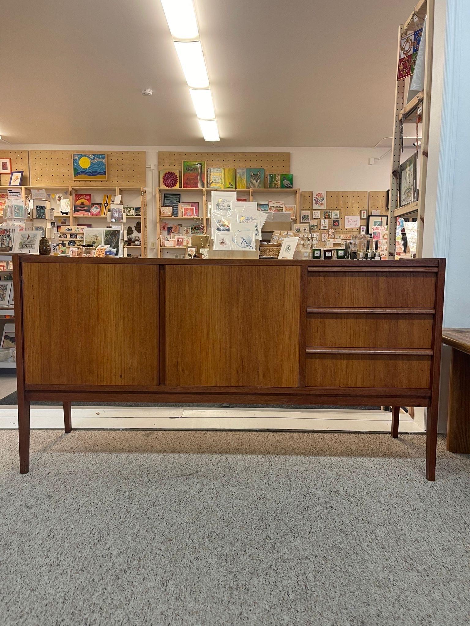 This sideboard has three sections, two for cupboard space and the third contains three dovetailed drawers. Possibly Teak with wood carved handles. No Makers mark. Vintage Condition Consistent with Age as Pictured.

Dimensions. 60 W ; 17 D ; 32 H