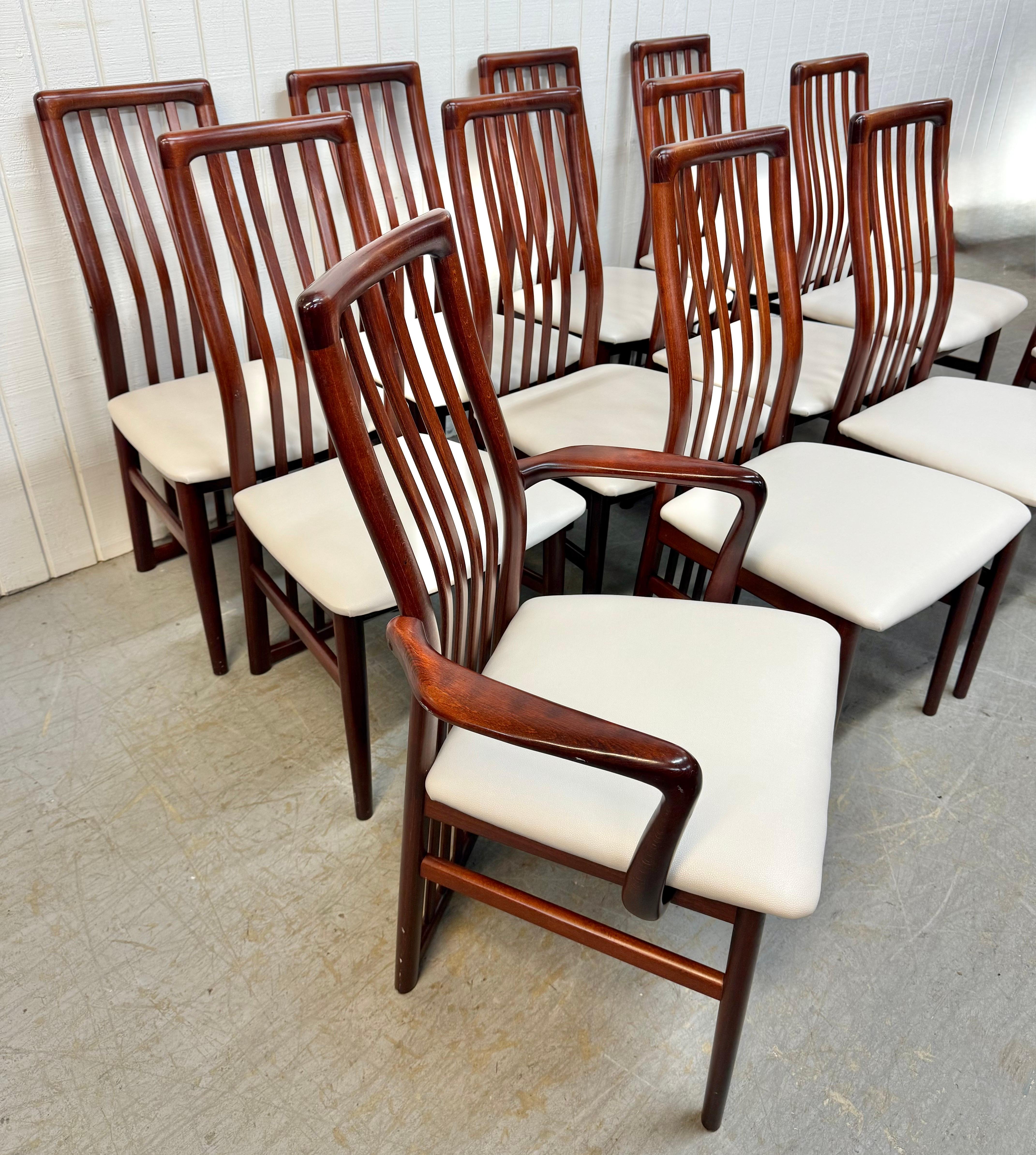 Cette offre concerne un ensemble de douze chaises de salle à manger en bois de rose vintage danois moderne. Avec un dossier en fuseau ondulé, deux chaises à bras, dix chaises d'appoint, de nouveaux sièges rembourrés en vinyle blanc, des pieds