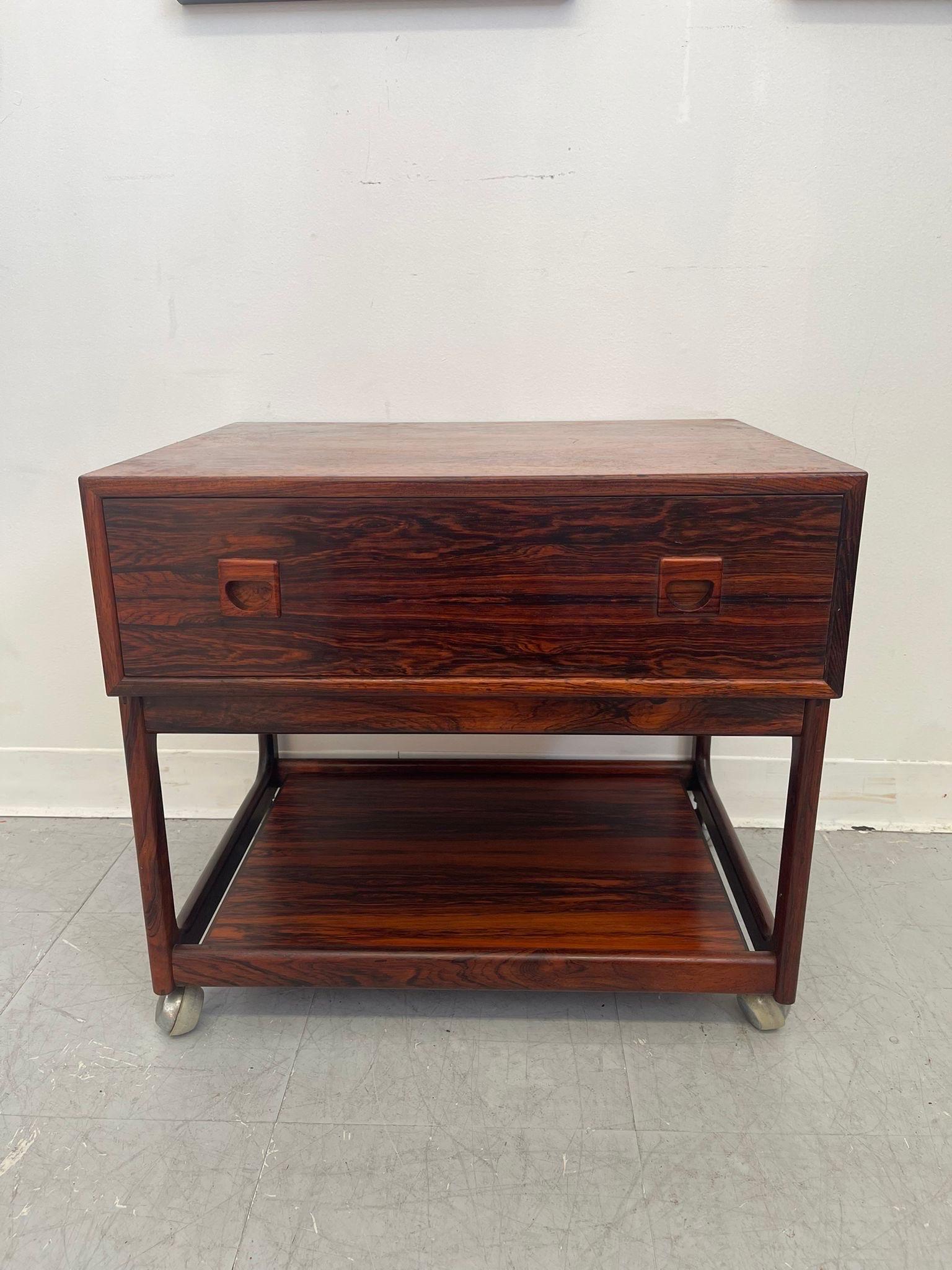 This is a classic Danish Modern design, especially in regards to the wood carved handles. Single dovetailed drawer with dividers above open shelf space.Beautiful rosewood grain. Finished Back. Vintage Condition Consistent with Age as
